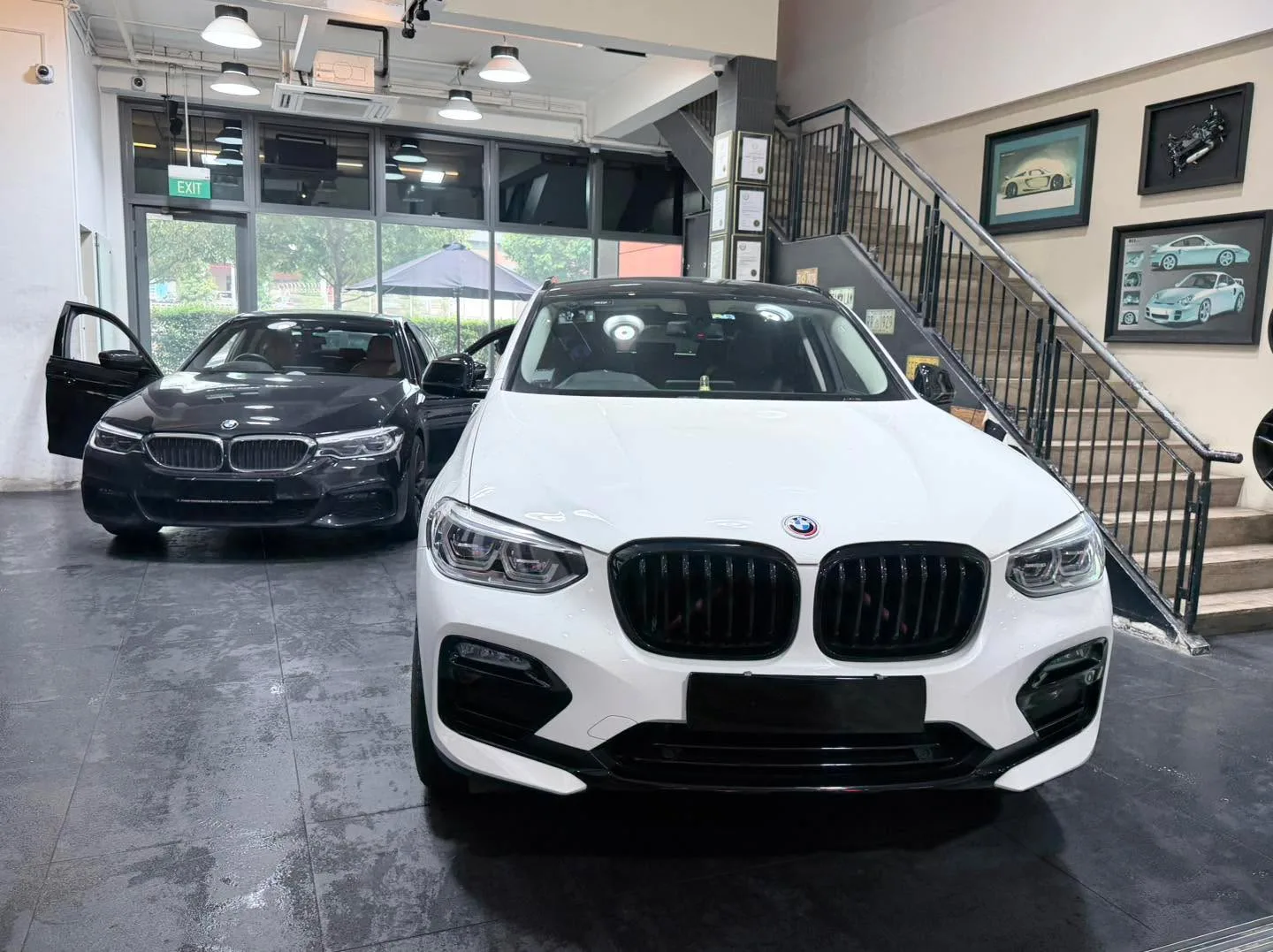 A white BMW X4 SUV and black BMW 5 Series saloon indoors.