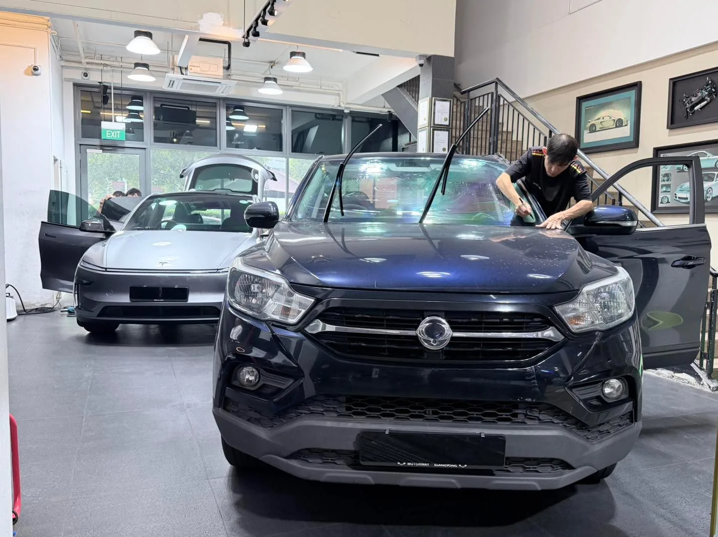 Staff applying window tint to a dark-coloured compact SUV with doors open.