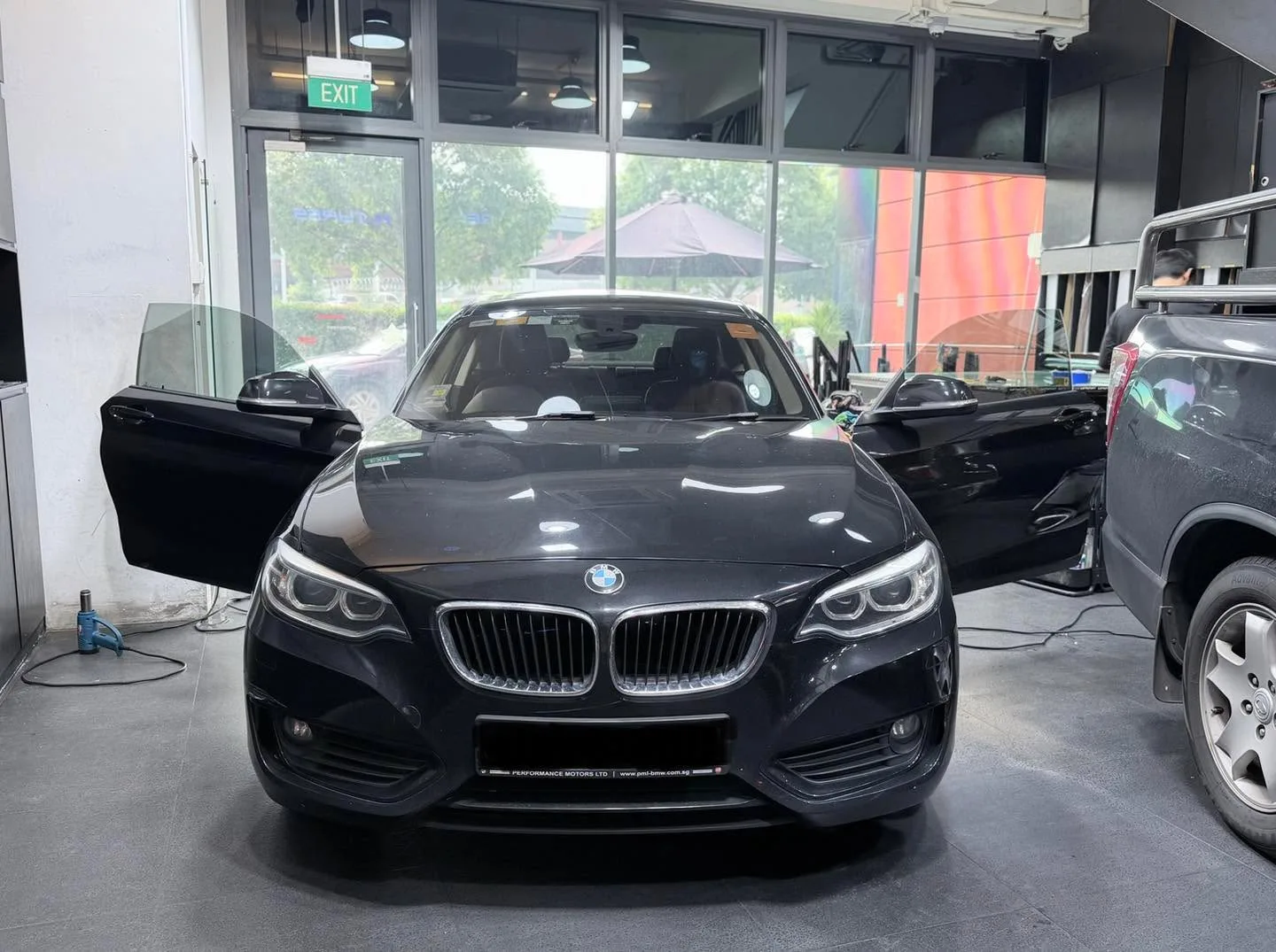 A black BMW saloon with open doors during tinting application.