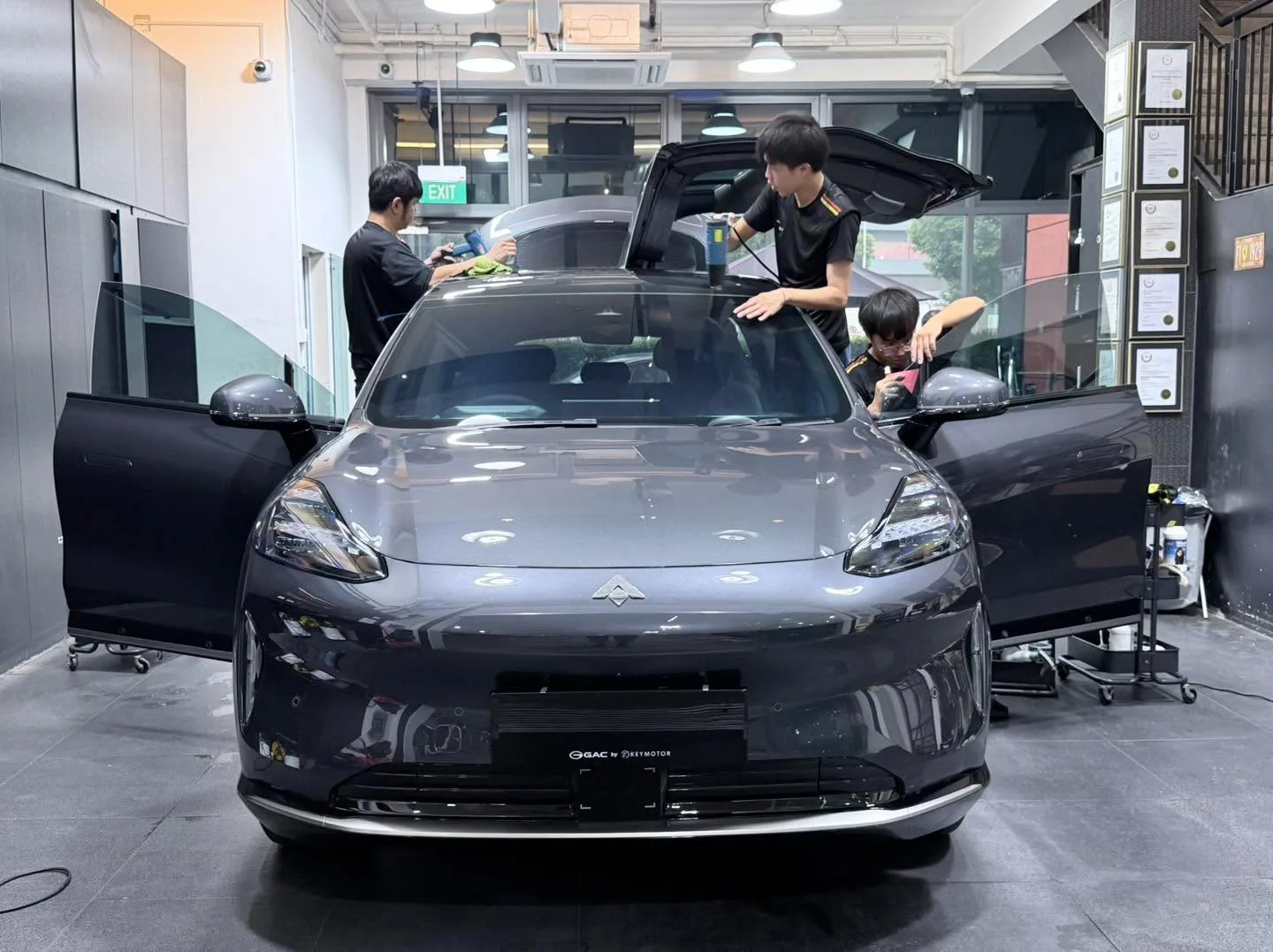 Staff working on a grey electric saloon with open doors and sunroof.