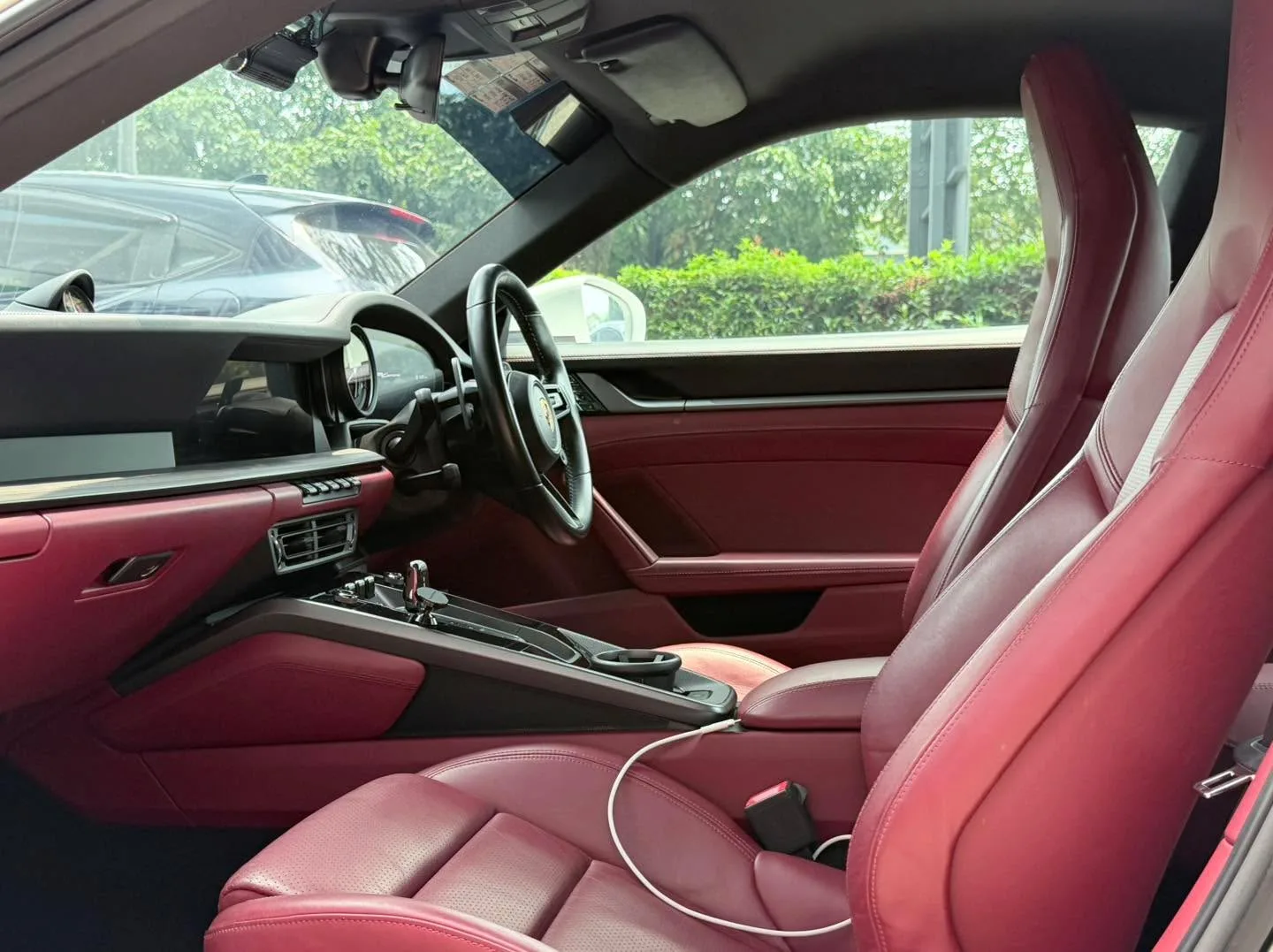 Interior view showing the driver's seat and dashboard of a Porsche with burgundy and cream leather upholstery.