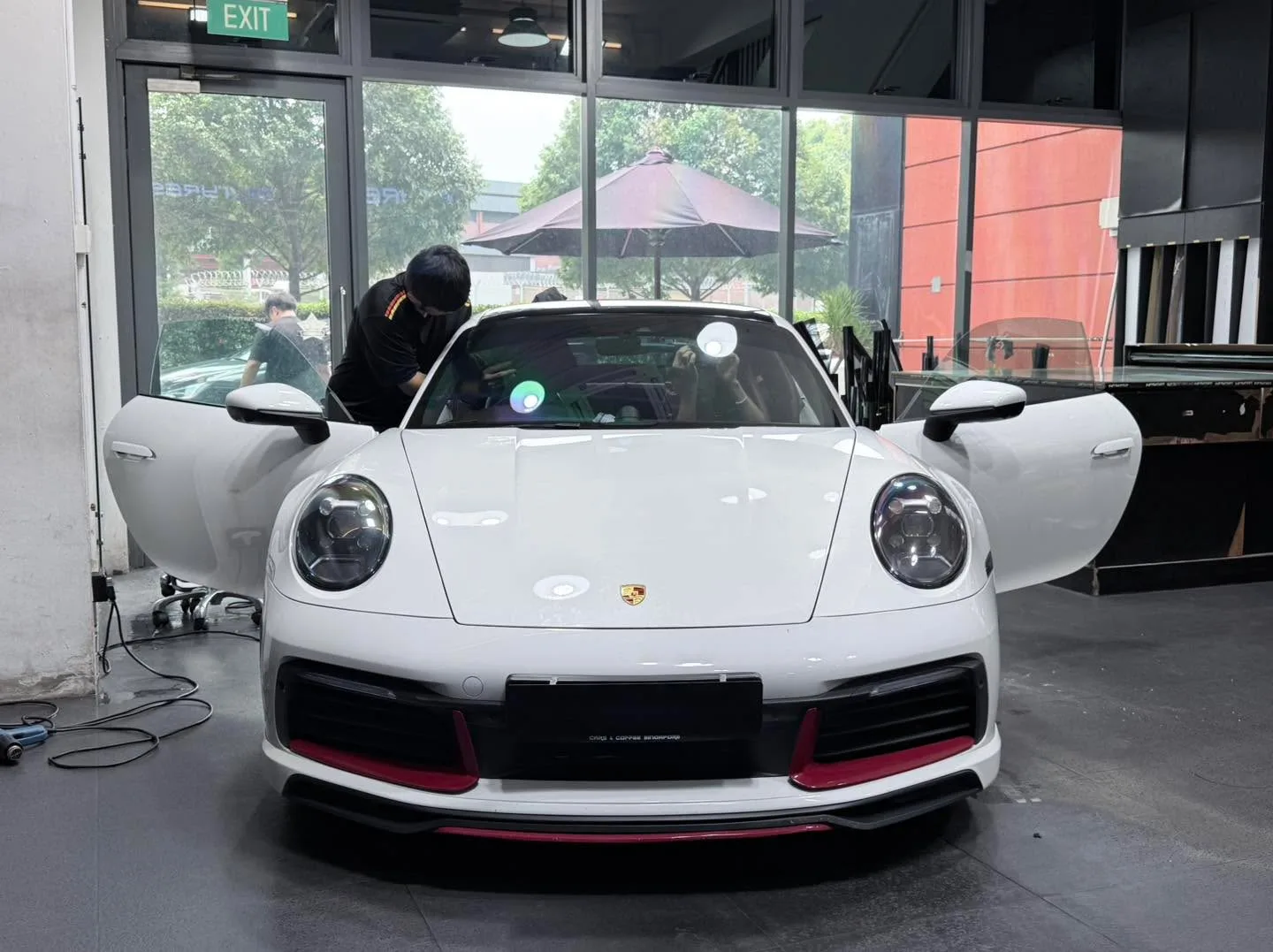 A white Porsche 911 with its doors open inside the Infratint workshop, with a technician working on the windows.