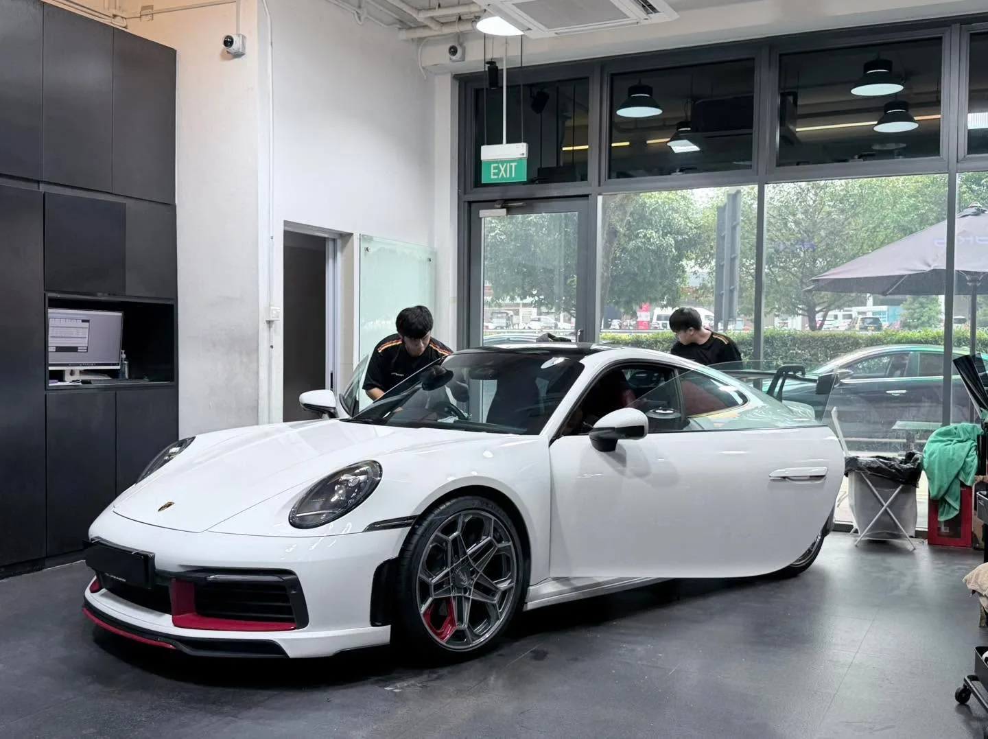 A white Porsche 911 inside the workshop with two technicians working on the windows.