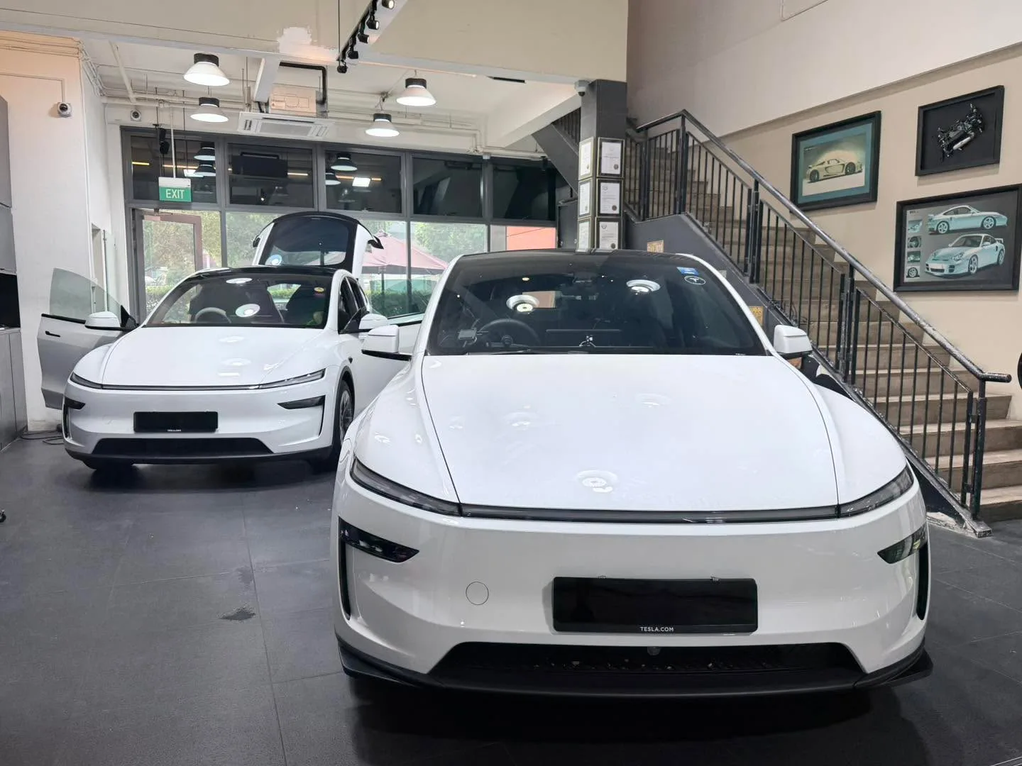 Two white Tesla electric vehicles parked in the workshop, one sedan and one sports car with gull-wing doors.