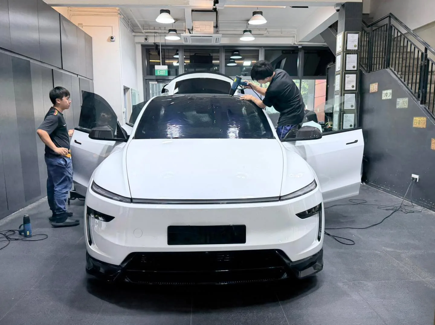 A white Tesla sports car with its gull-wing door open, being worked on by two technicians applying window tint.
