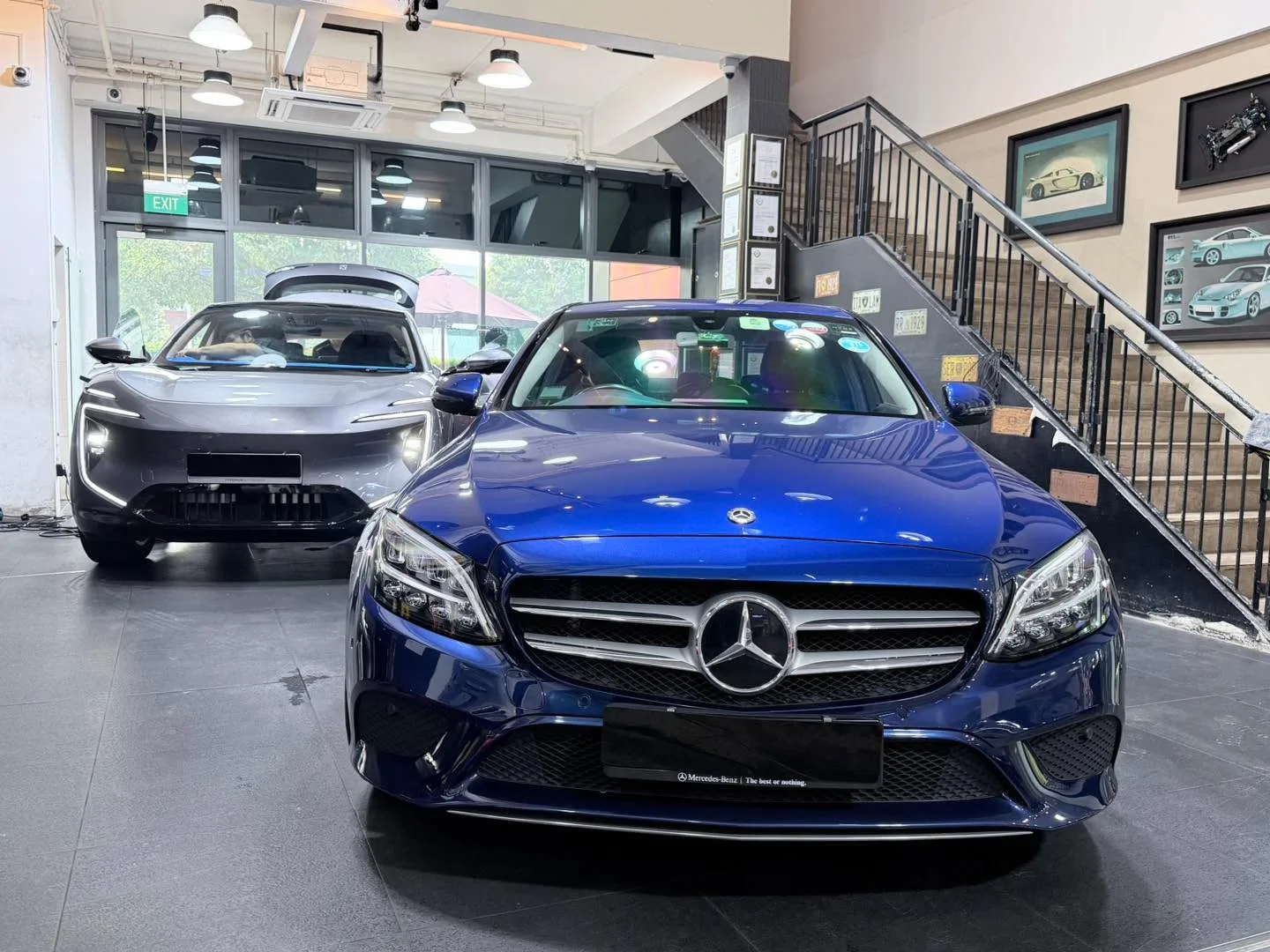 A blue Mercedes-Benz sedan in the foreground, parked indoors at the workshop with a grey Avatr visible behind it.