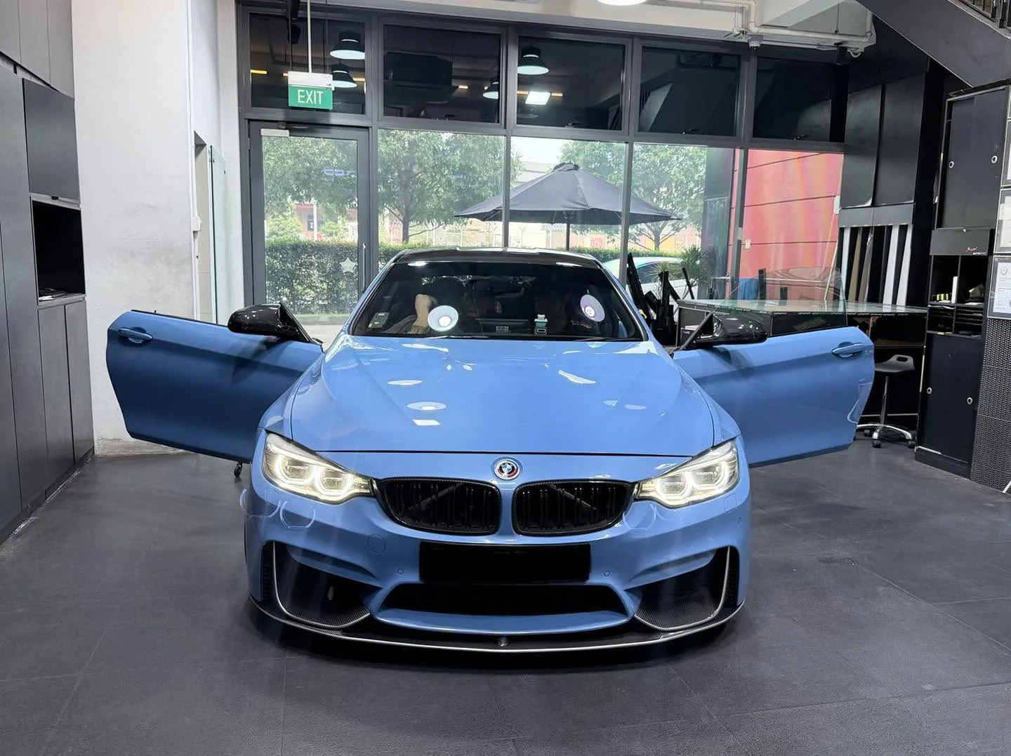A bright blue BMW M4 coupe with both doors open, parked indoors at the workshop.