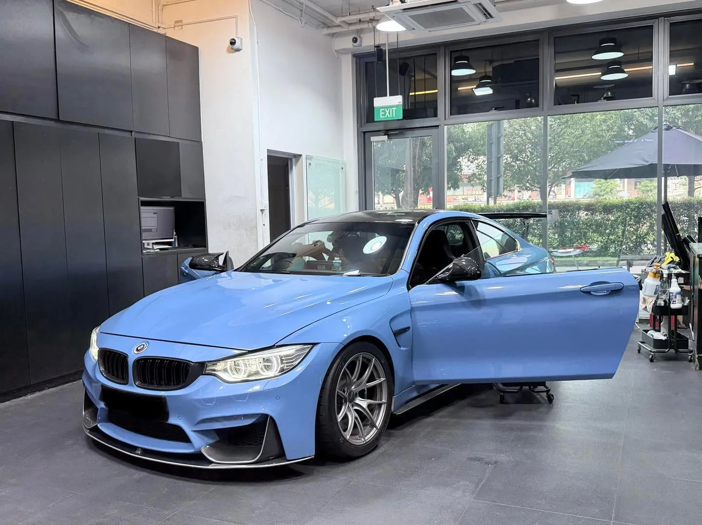 A bright blue BMW M4 coupe facing forward with doors open, in the workshop interior.