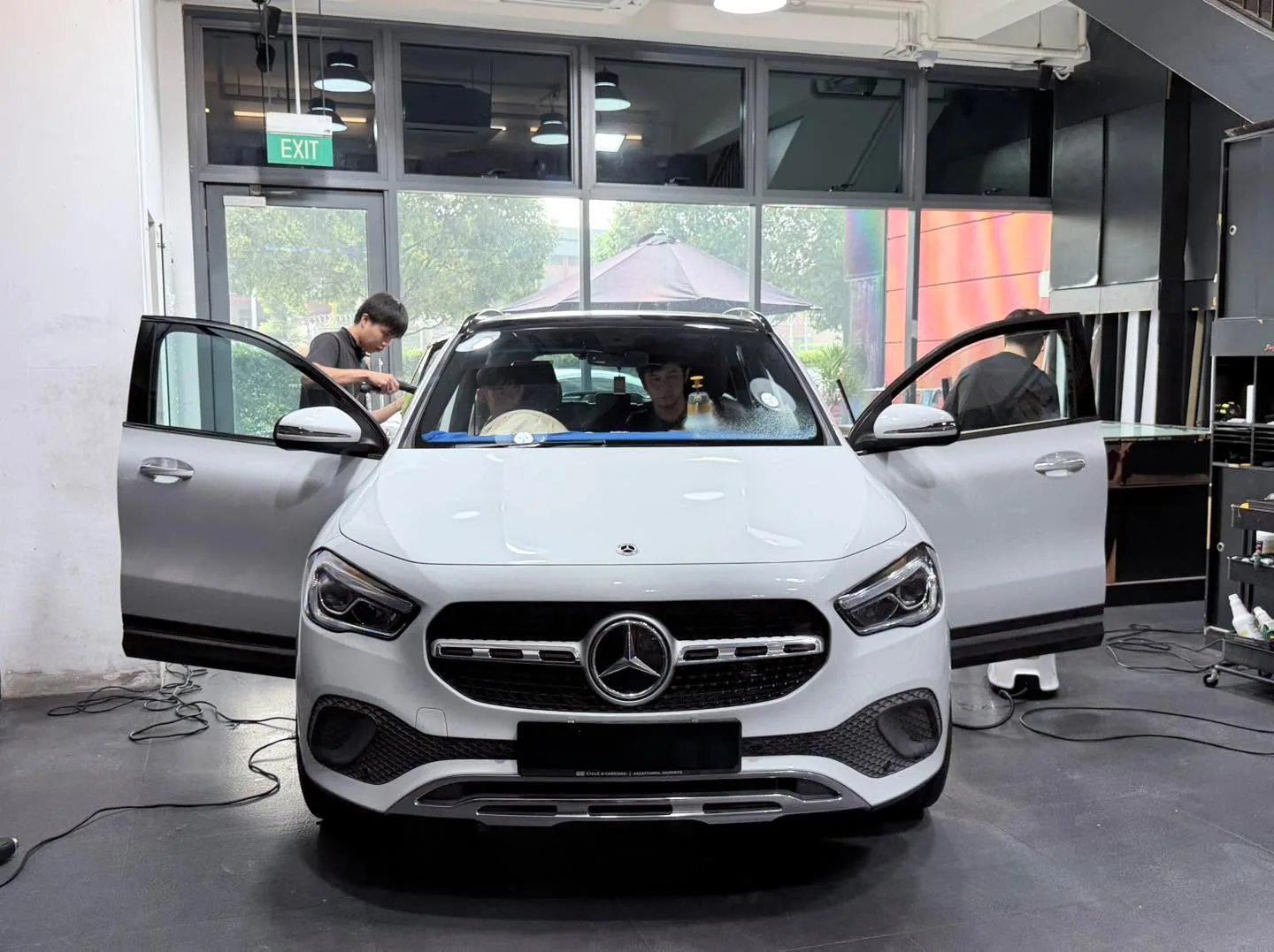A white Mercedes-Benz SUV with both doors open, showing tinting in progress at the workshop.