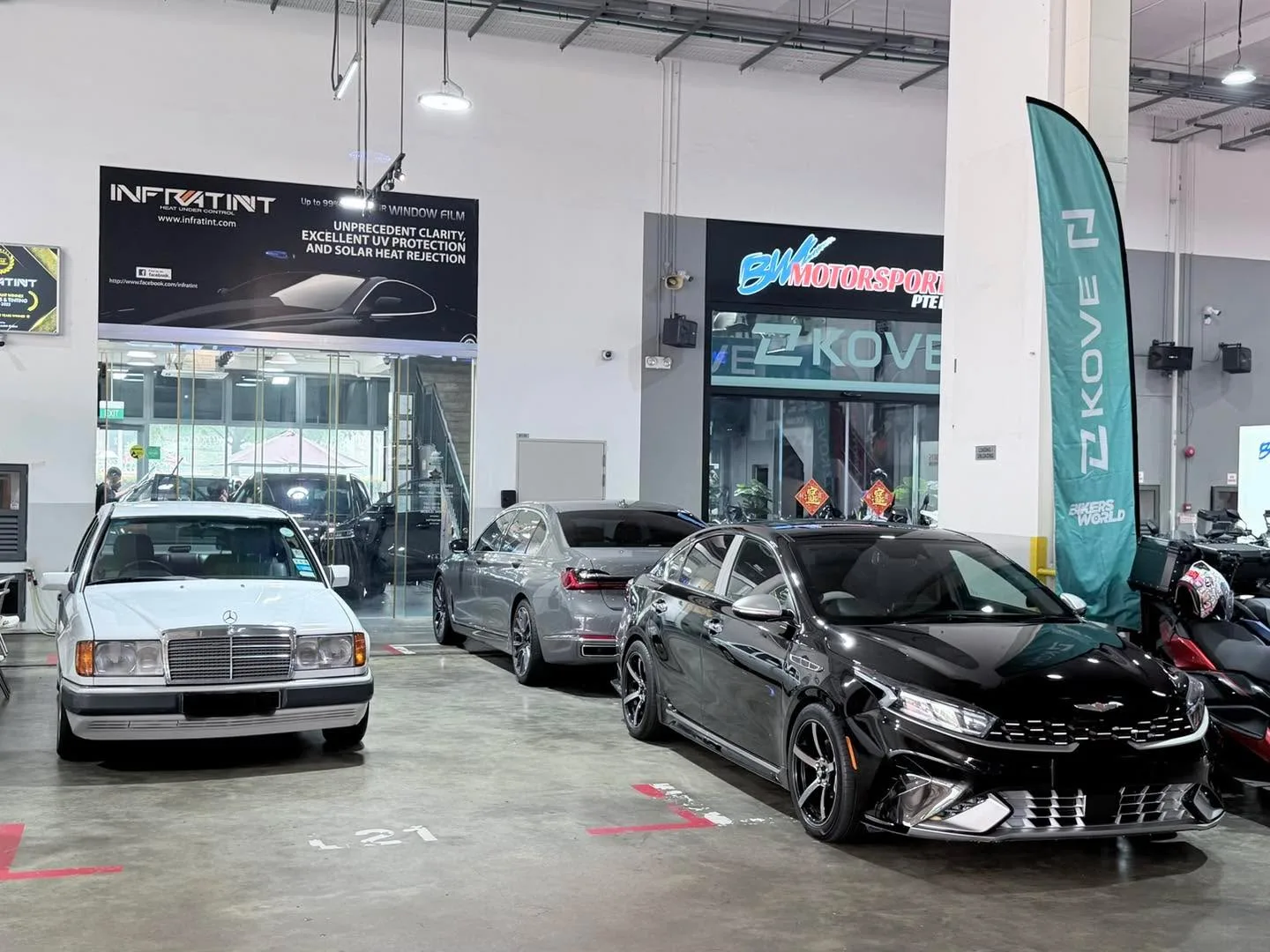 White Mercedes-Benz, black Kia, and grey sedan parked in workshop.