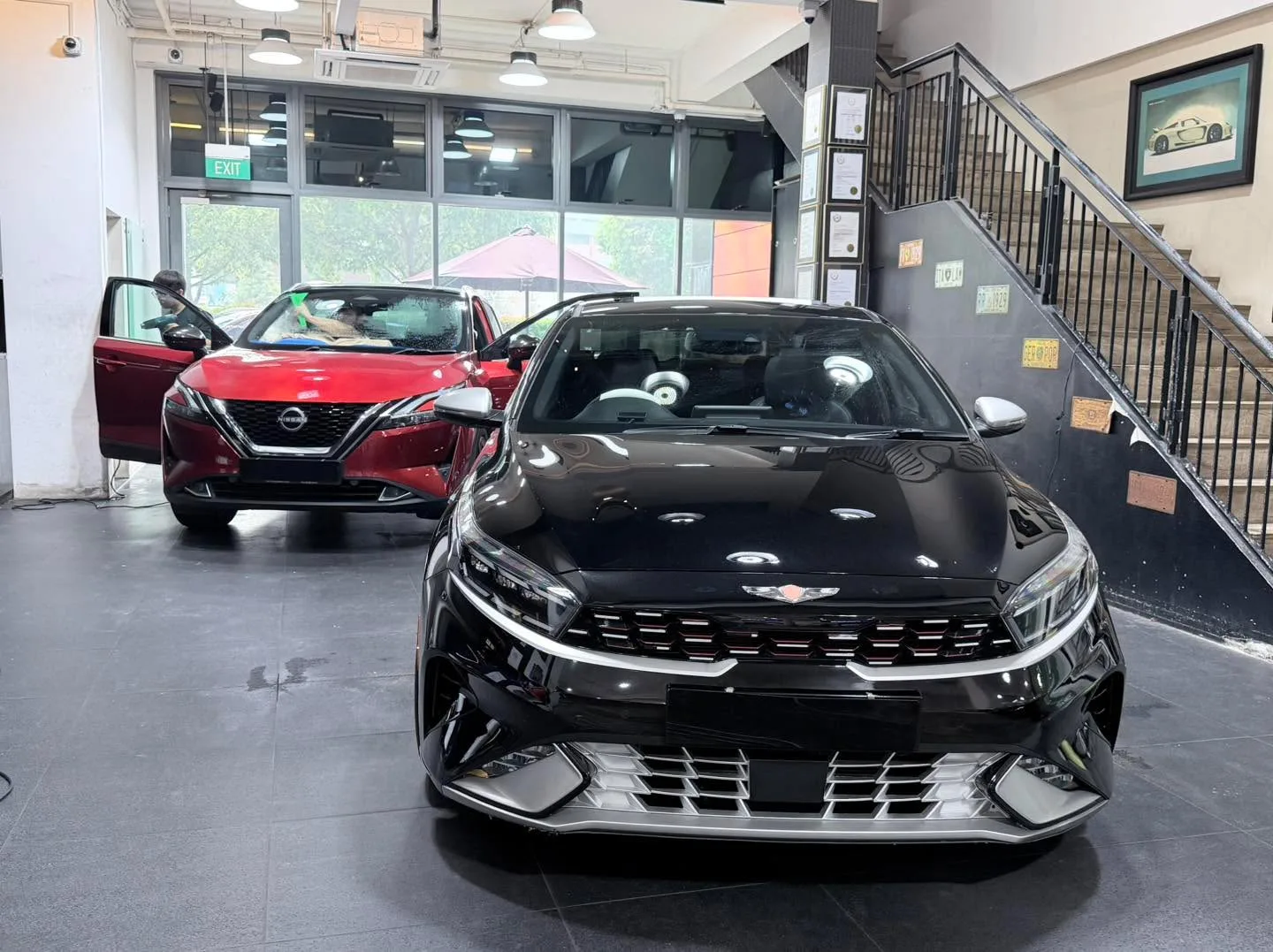 Black Kia Cerato and red Nissan Qashqai, doors open.