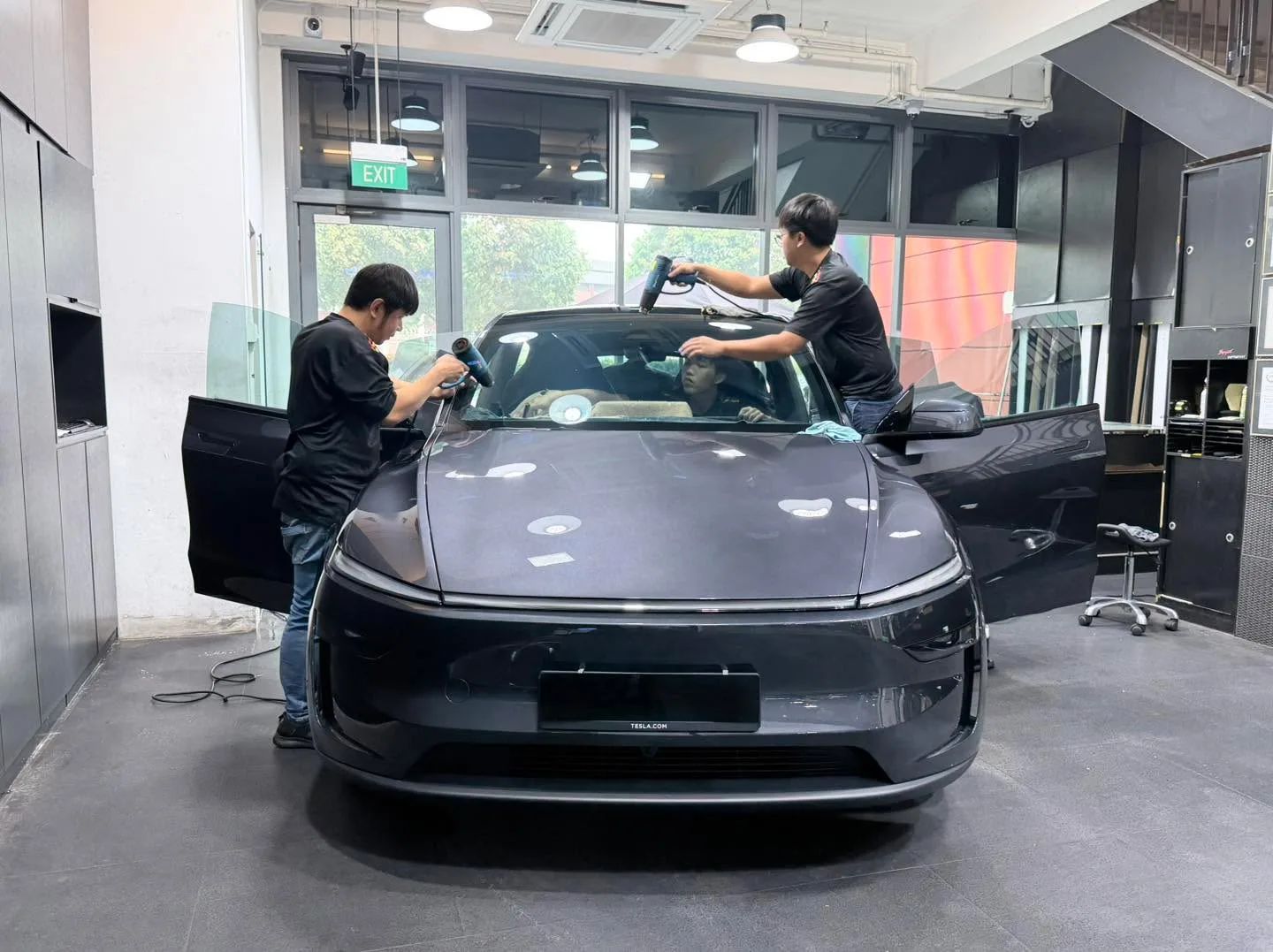 Black Tesla Model Y Juniper with two technicians applying film to windscreen.