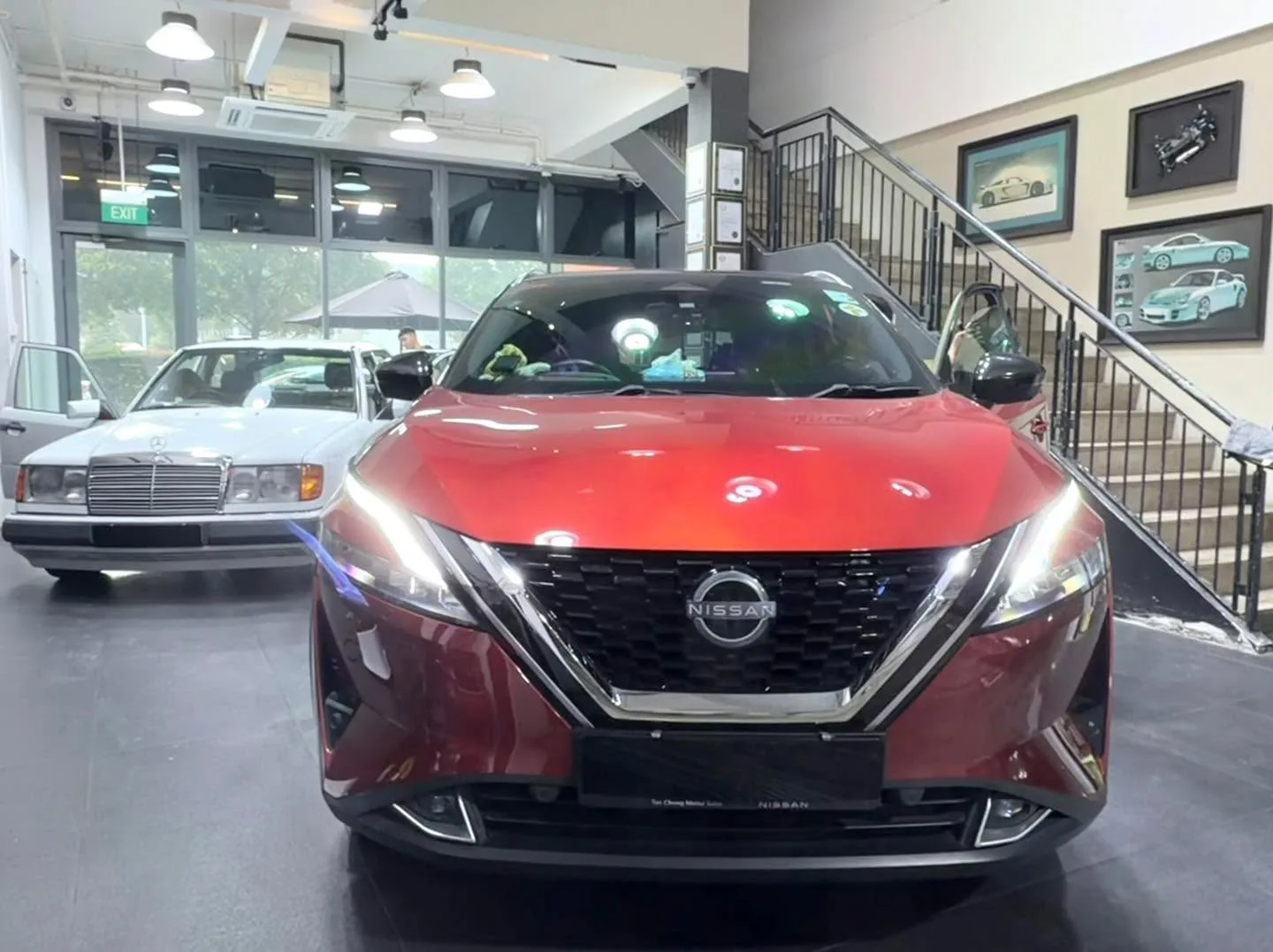 Red Nissan Qashqai front view with white Mercedes-Benz behind.