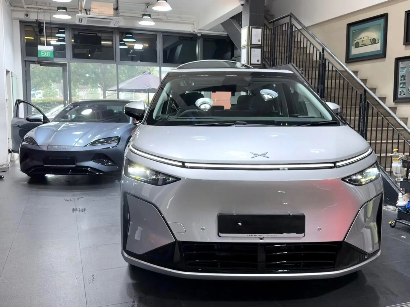 White XPENG X9 electric MPV and dark Tesla indoors with glass storefront behind.