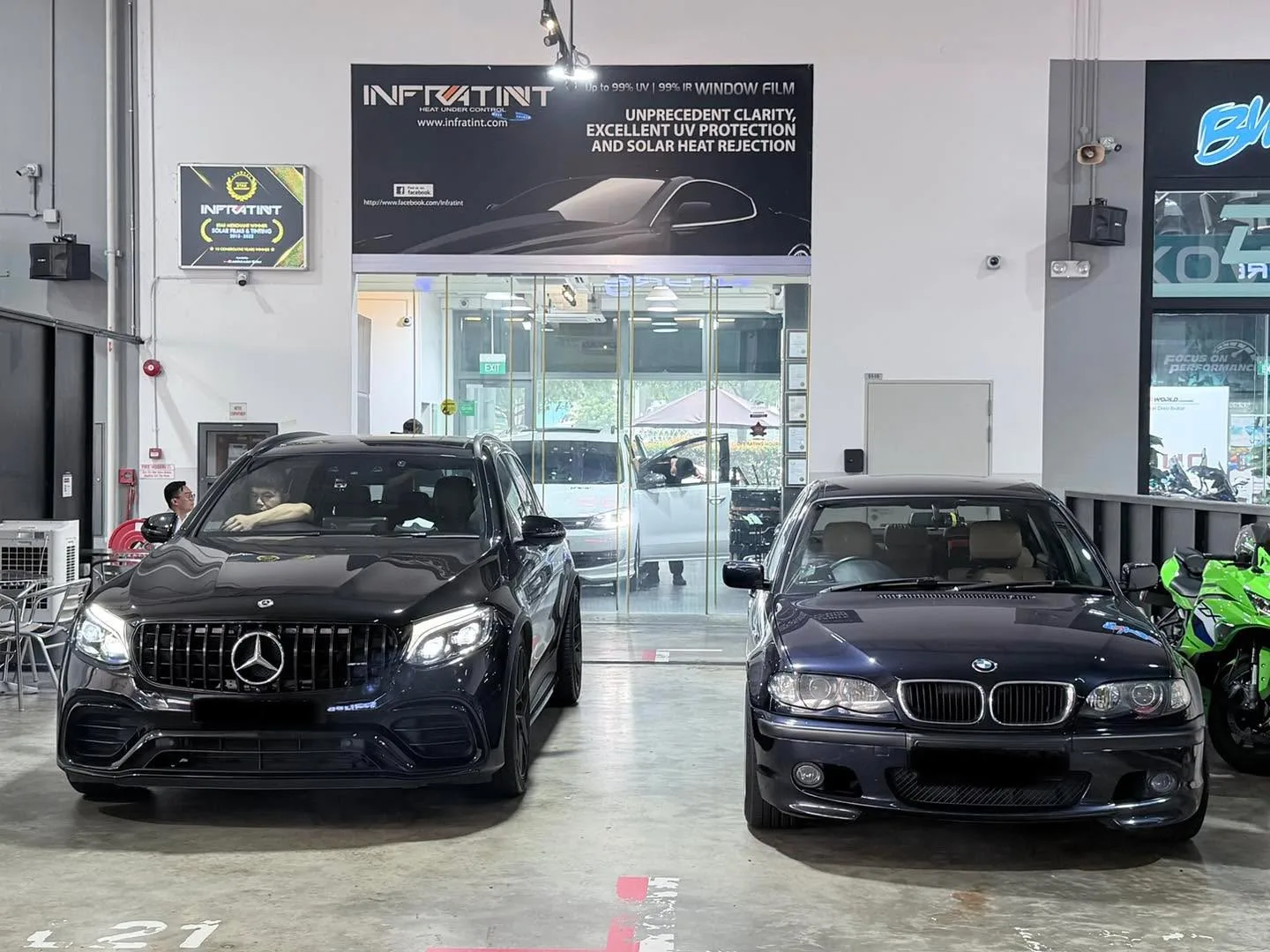 A black Mercedes-Benz GLC and a dark blue BMW 3 Series parked side by side in the workshop.