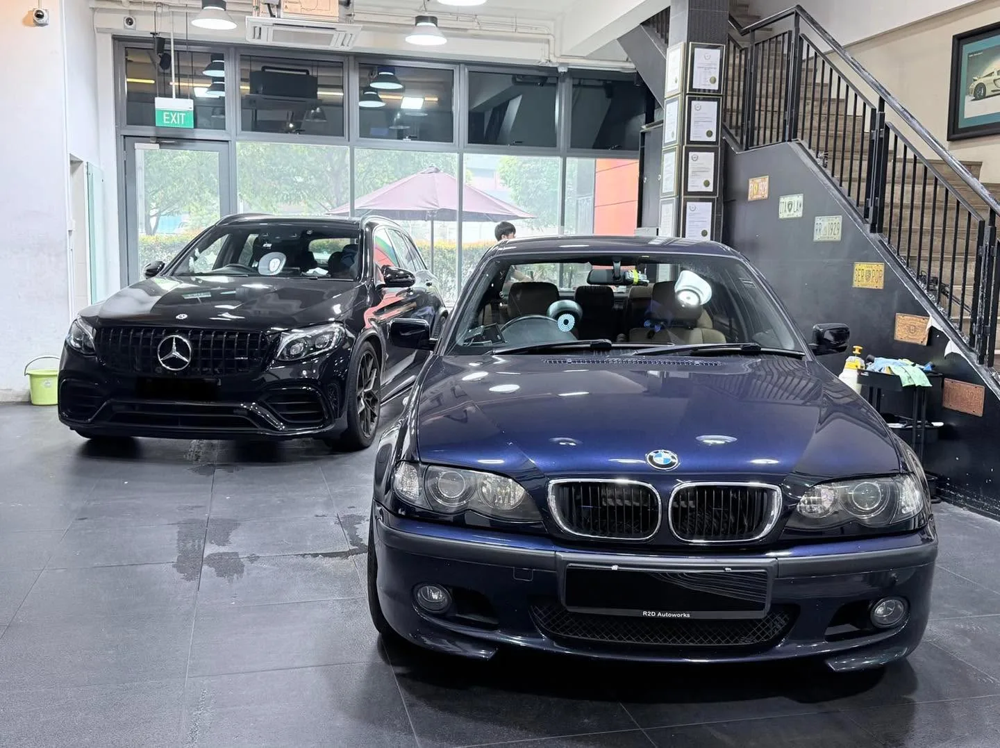 The same black Mercedes-Benz GLC and dark blue BMW 3 Series in the workshop bay with staff nearby.