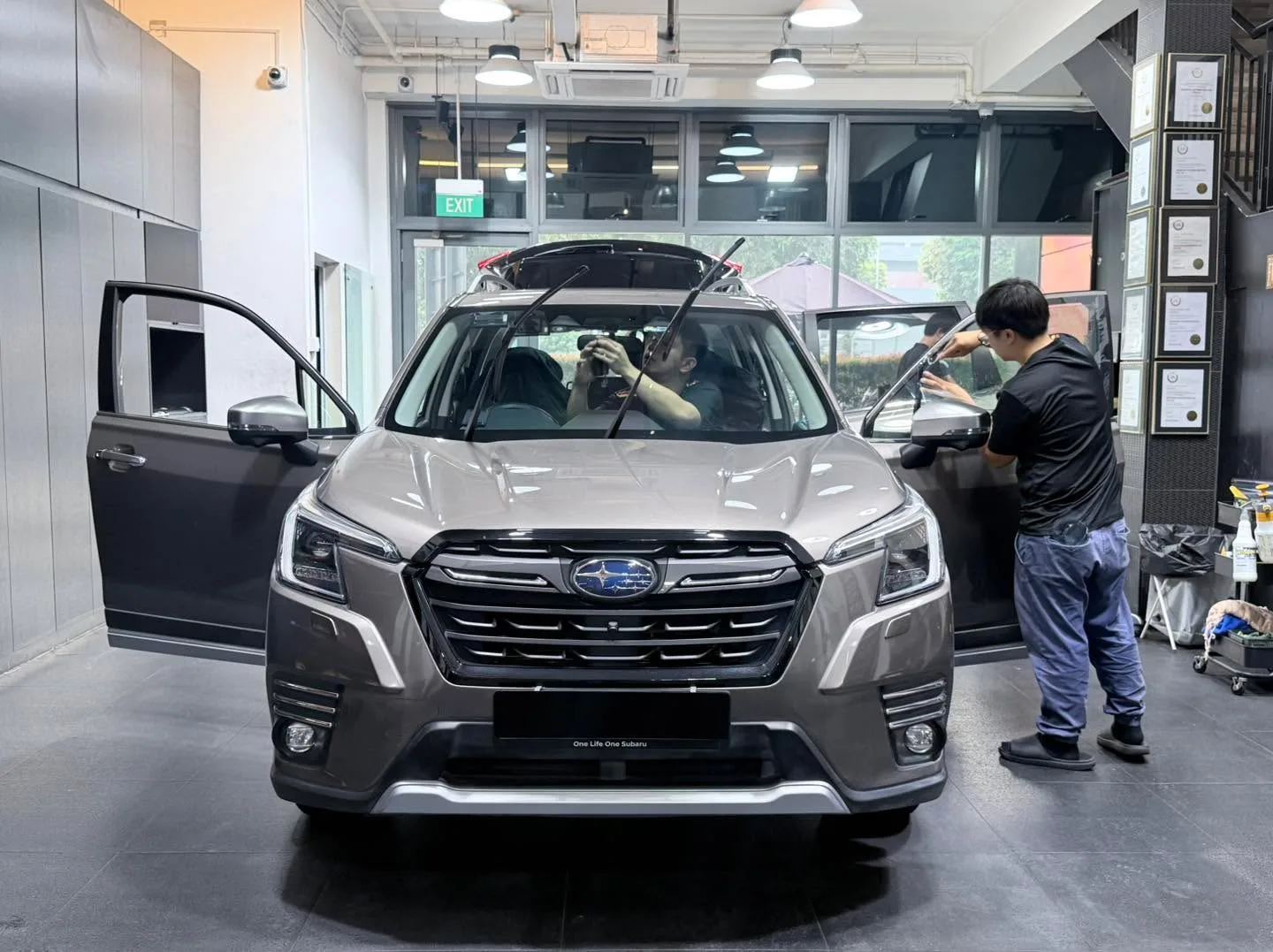 A silver Subaru Forester SUV with doors open, undergoing window tinting inside the workshop.