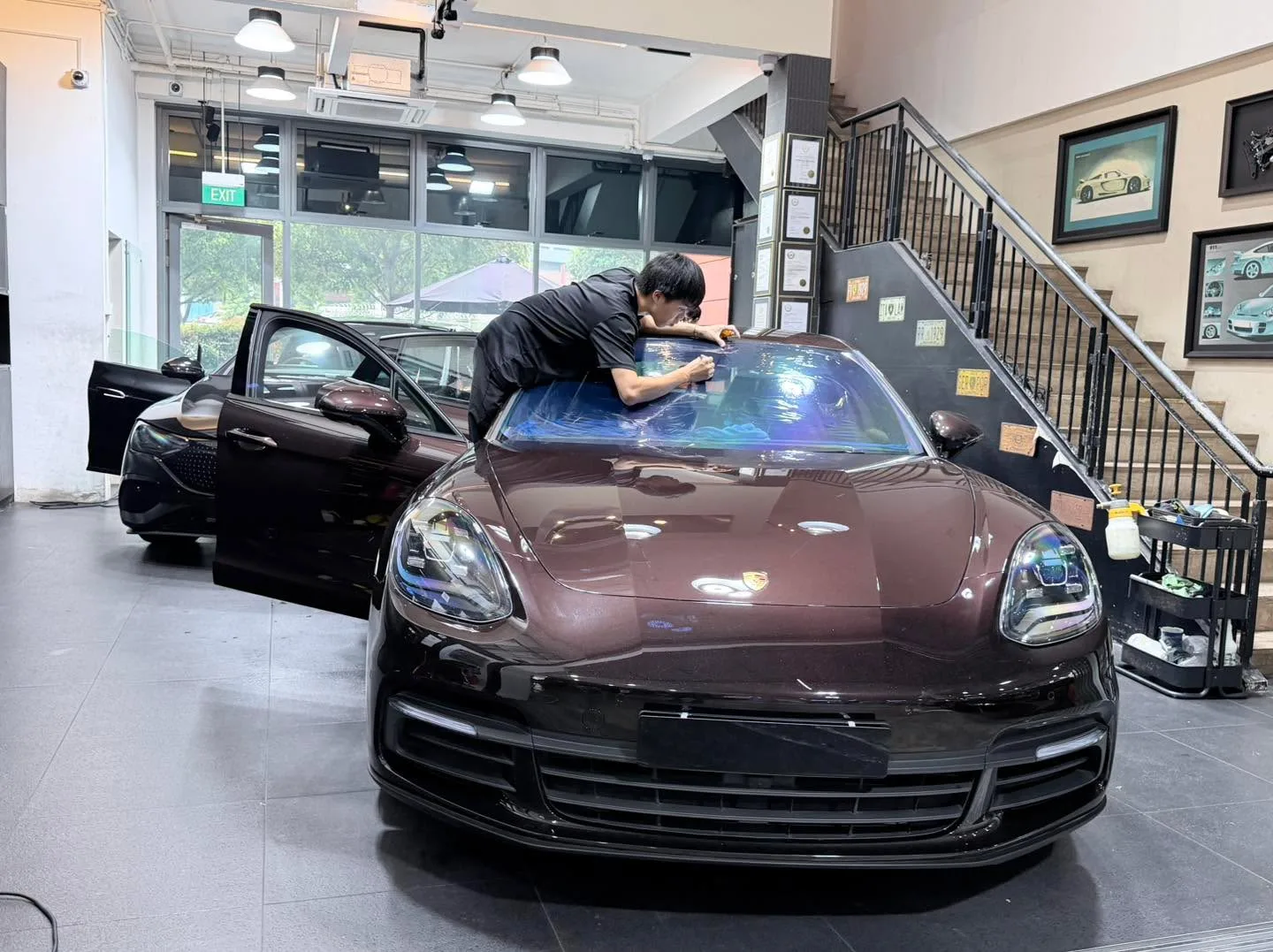 A dark burgundy Porsche sports car with its roof panel being tinted by a technician.