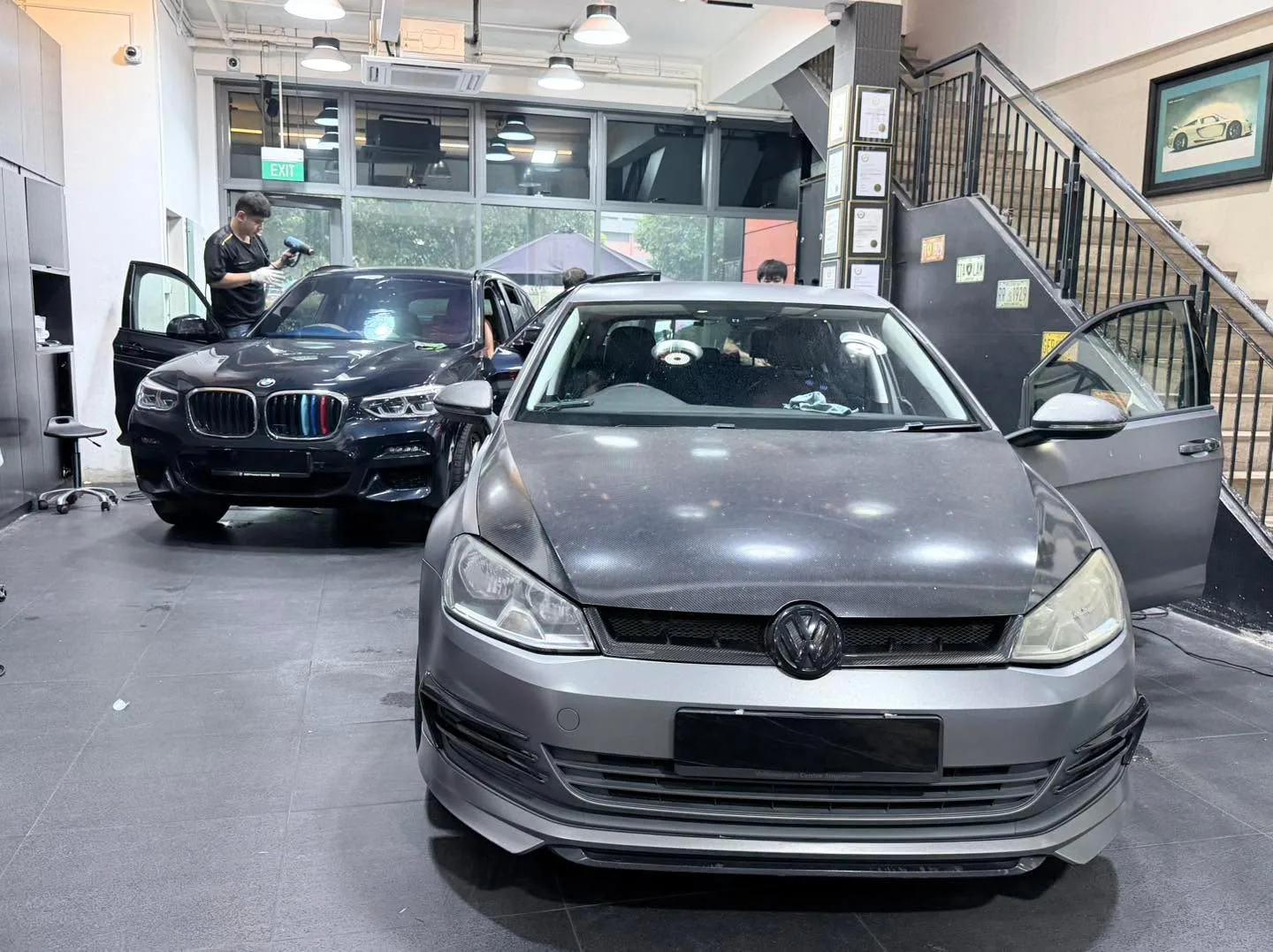 A silver Volkswagen Golf hatchback in the foreground with a black BMW X3 SUV behind, both in the workshop.
