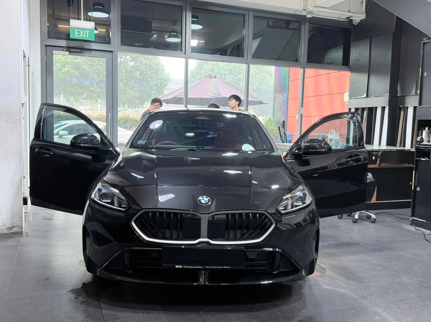 A black BMW 116 with doors open in the workshop.