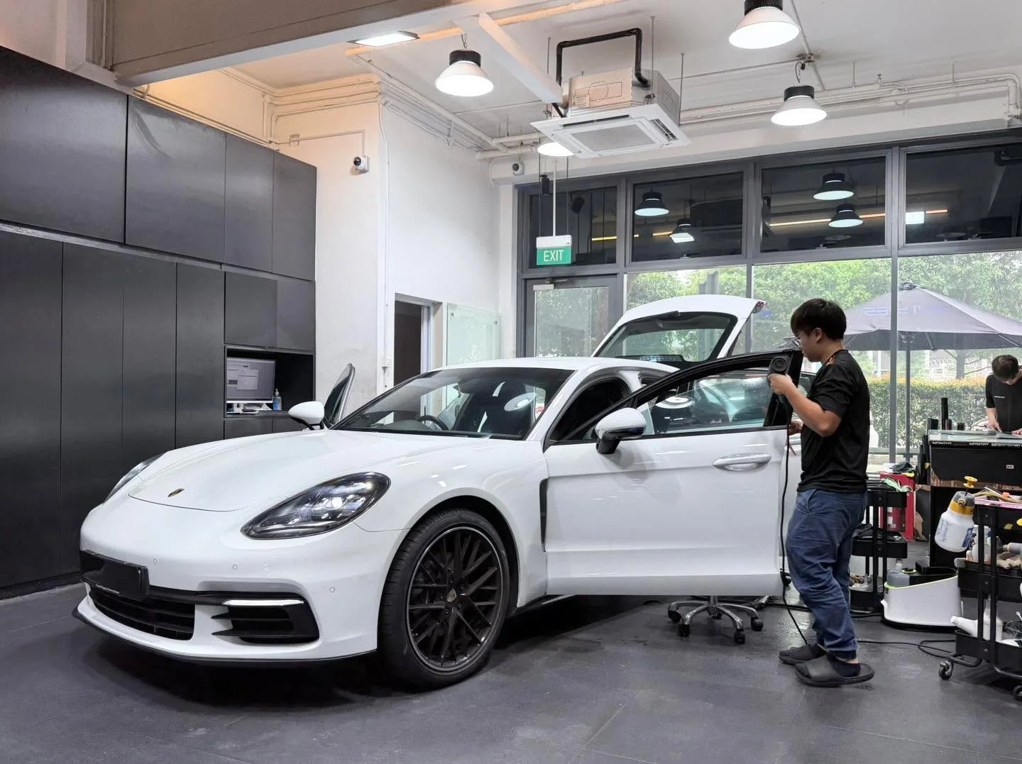 A white Porsche sports car with doors open, technician working on window.