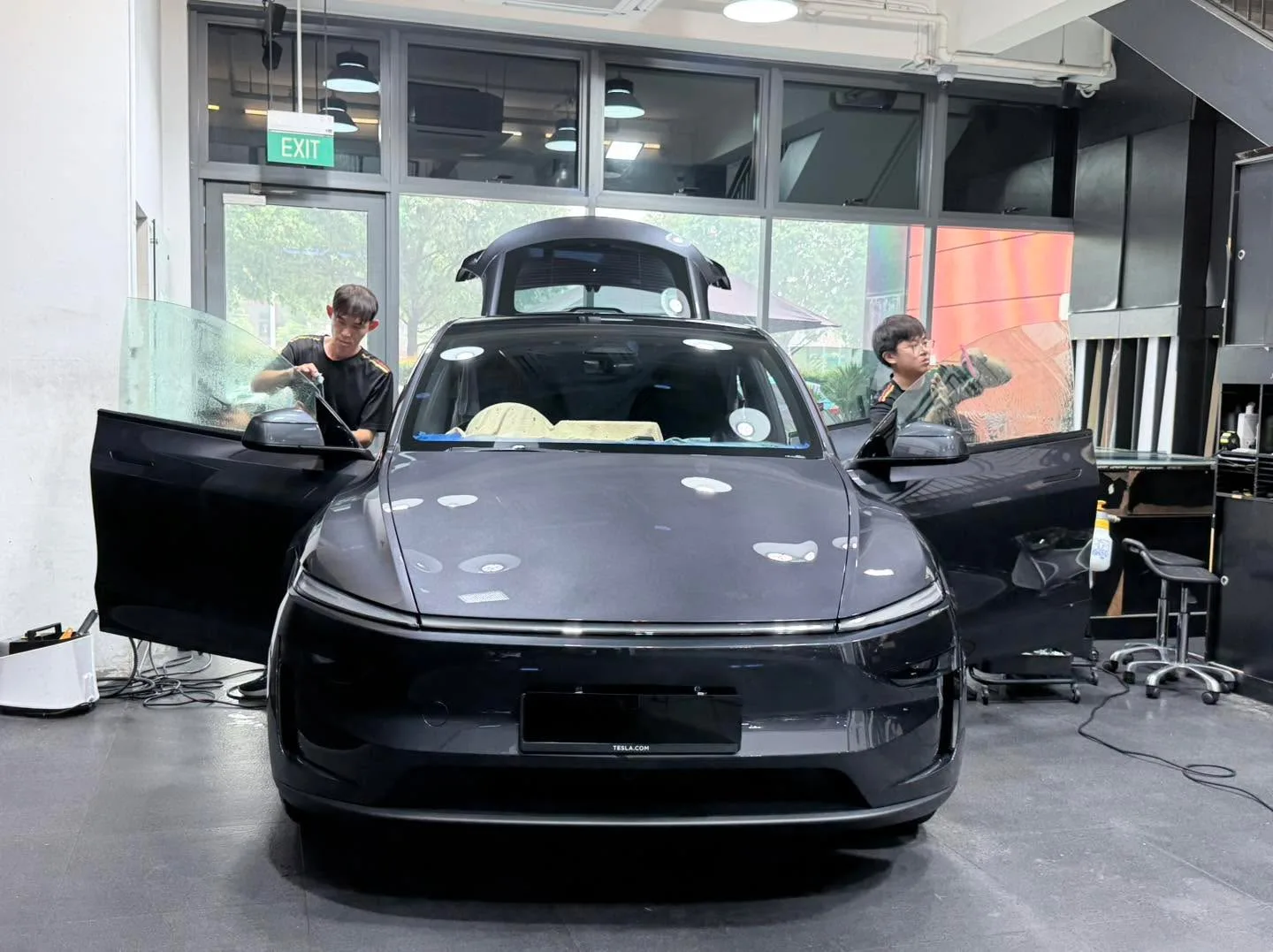 A black Tesla SUV with doors open, technicians working on windows.