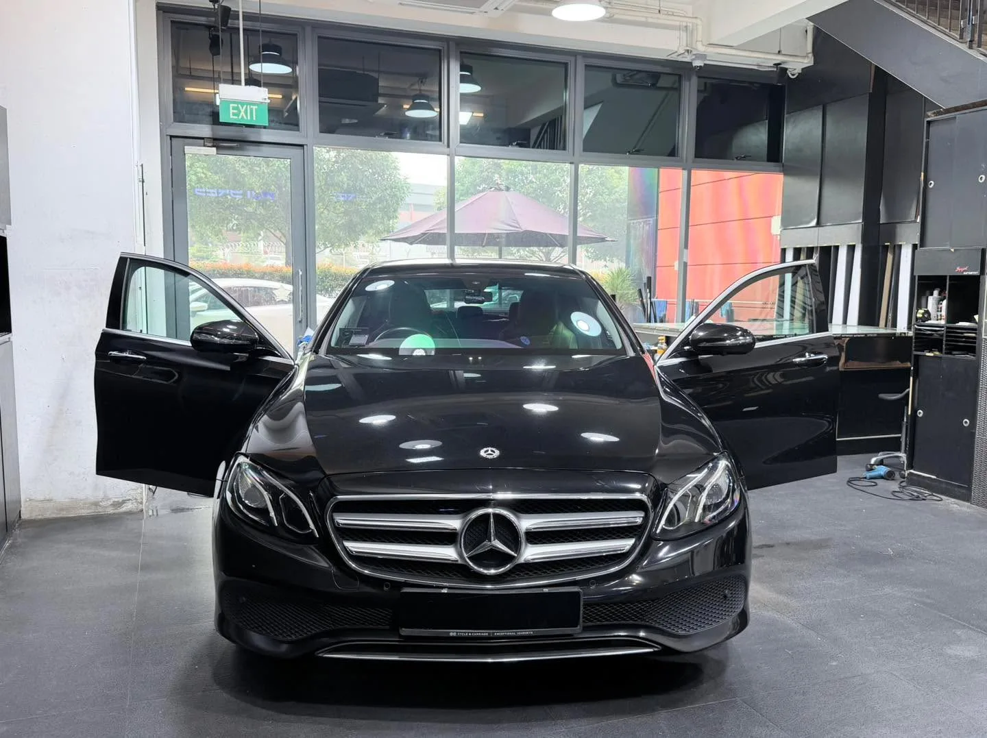A black Mercedes-Benz sedan with driver door open in the workshop.