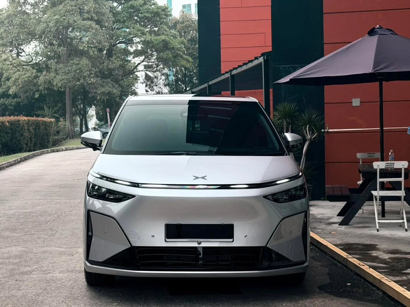 White XPENG X9 parked in front of a red and black building with trees visible in the background.