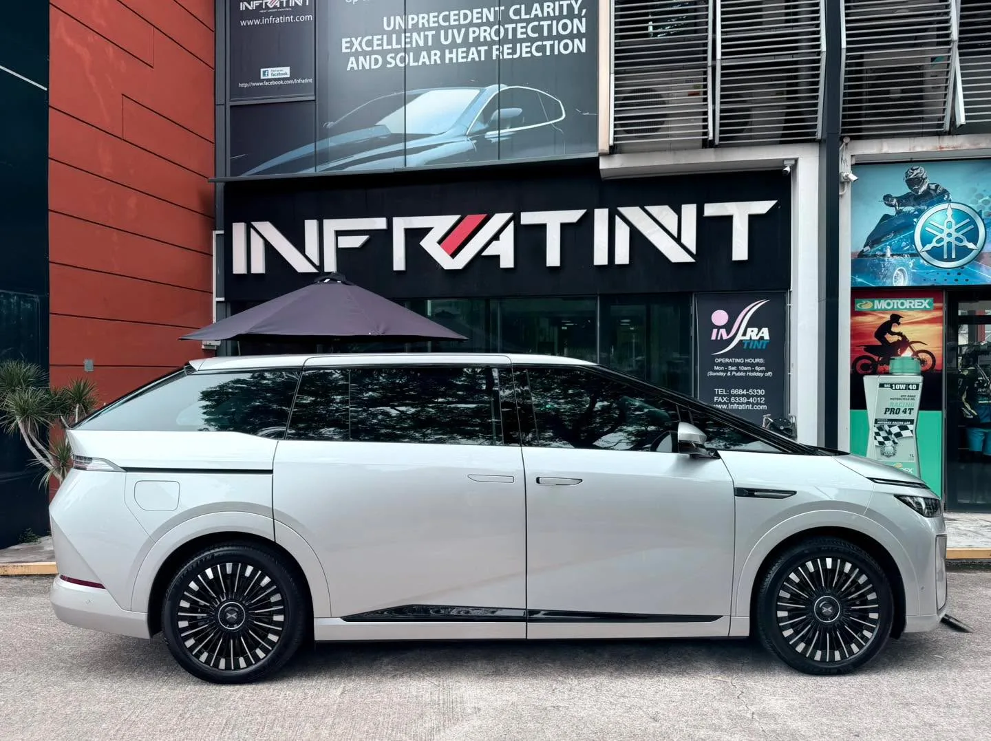 White XPENG X9 parked outside the Infratint workshop storefront with the Infratint logo visible behind.