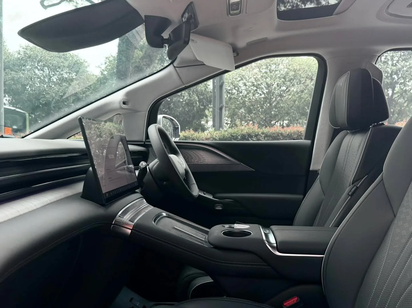 Interior of the XPENG X9 showing grey and black seats, steering wheel and tinted windows with trees visible outside.