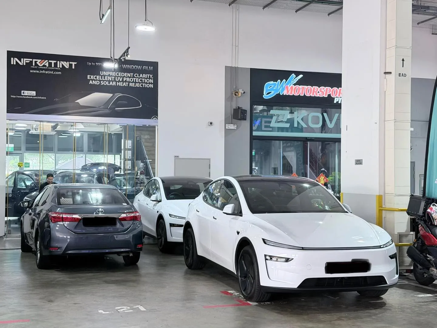 White Tesla electric SUV and grey Toyota sedan in the workshop.