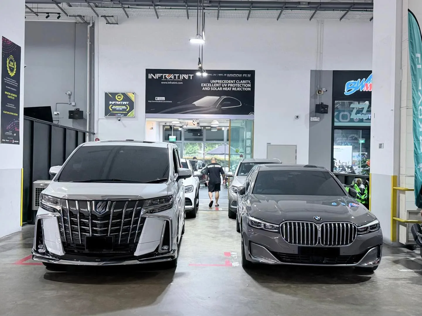 A white Toyota Alphard and grey BMW X3 parked side by side on the workshop floor.