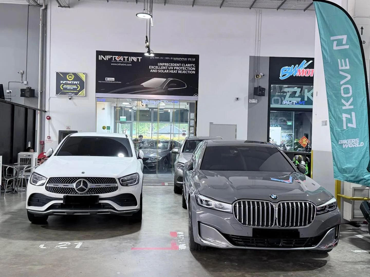 A white Mercedes-Benz GLC and grey BMW X3 parked side by side on the workshop floor.