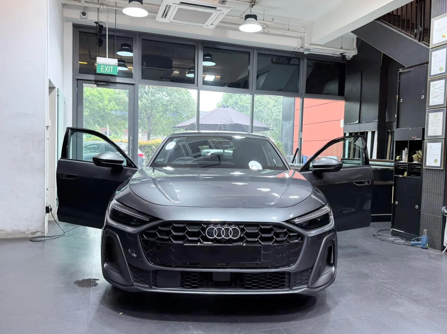 A dark Audi A5 with its doors open, parked in the workshop entrance area.