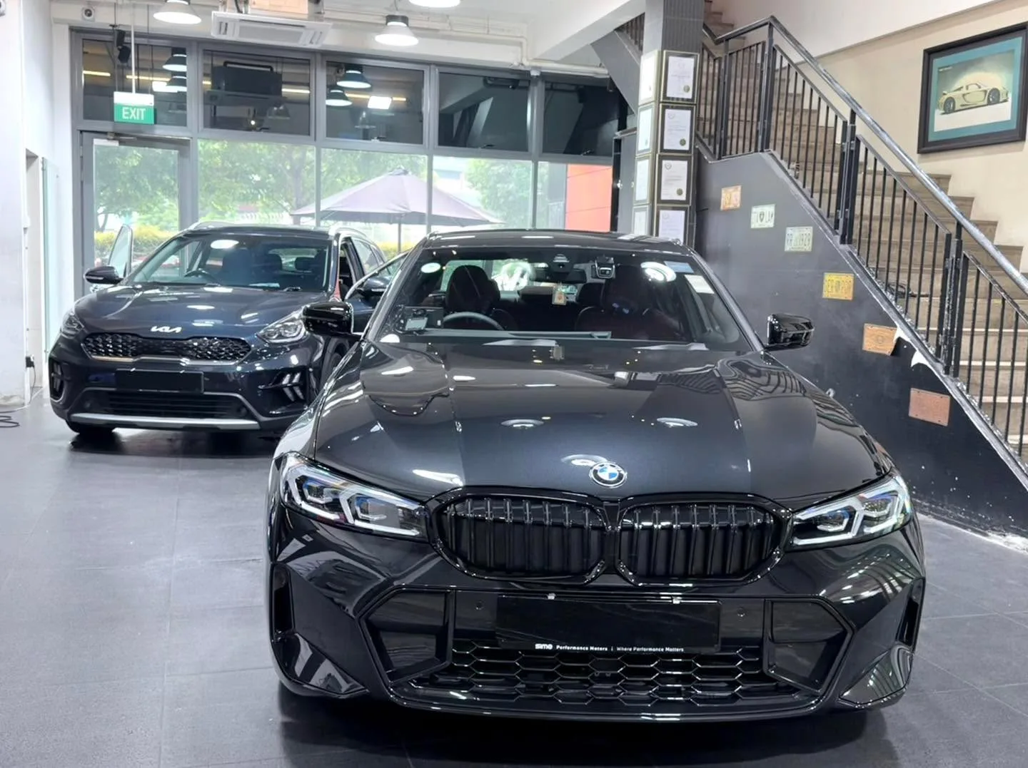 A black BMW with distinctive grille and white LED headlights, viewed head-on inside the workshop.