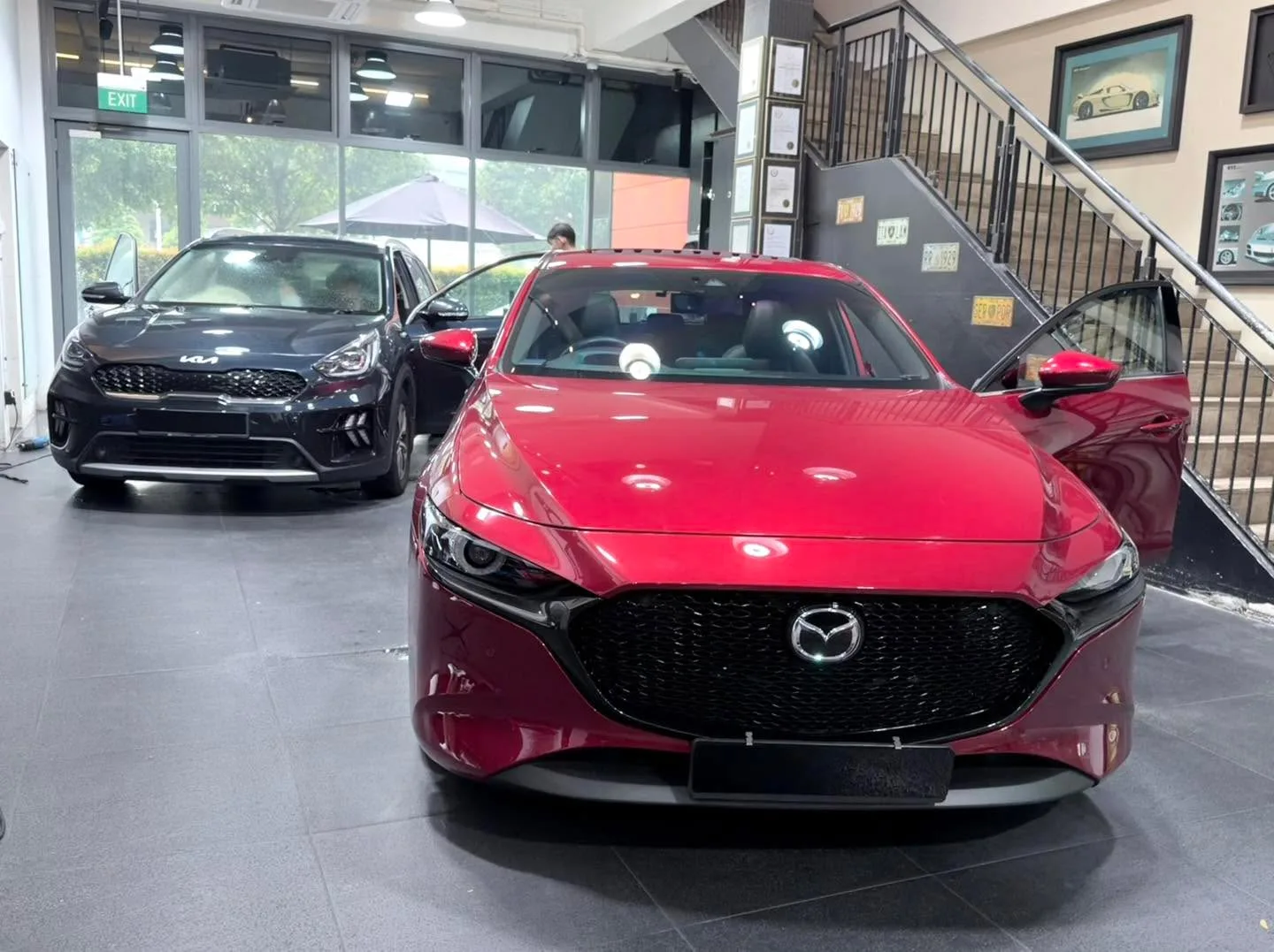 A red Mazda compact saloon with black grille, viewed from the front inside the workshop.