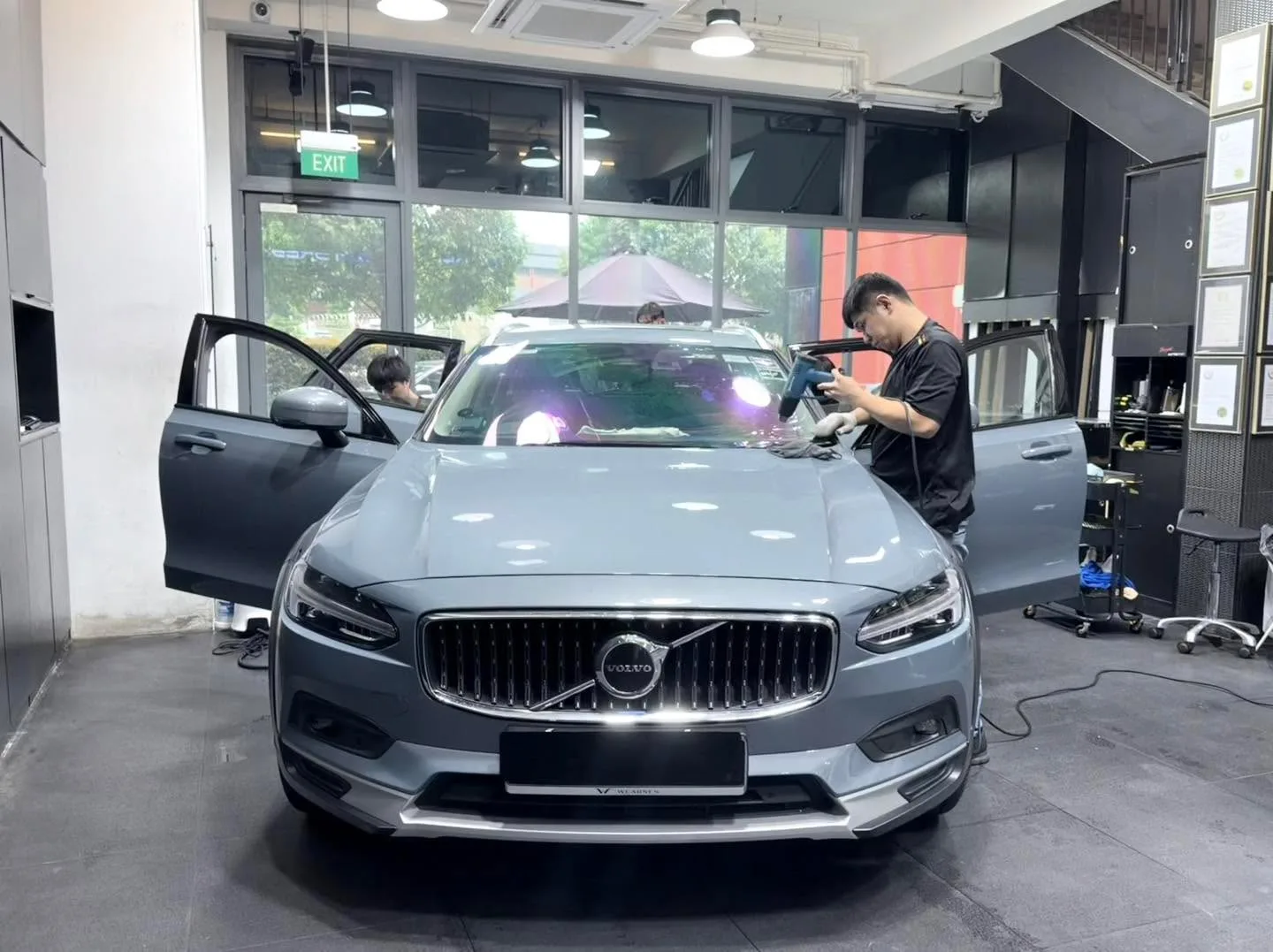 A silver Volvo estate car viewed head-on inside the workshop with technician attending to it.
