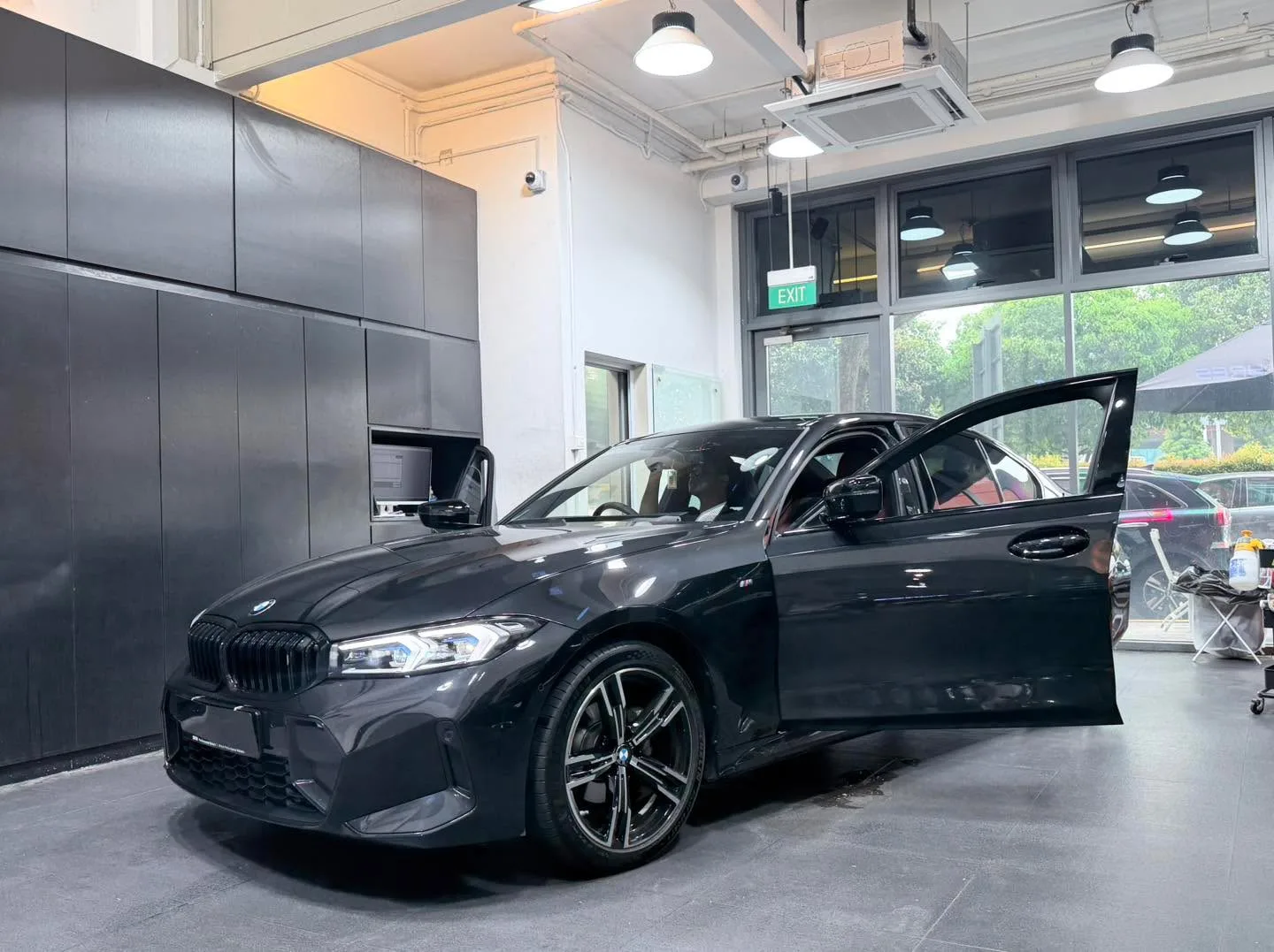 A black BMW compact saloon with M-spec styling and door open, viewed in three-quarter profile.