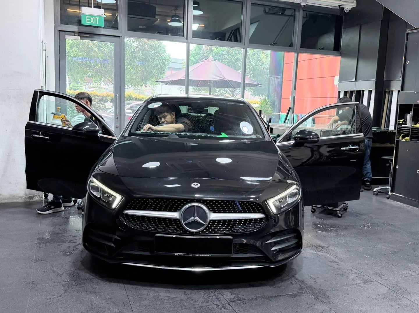 A black Mercedes-Benz compact saloon viewed straight-on with doors open in the workshop.