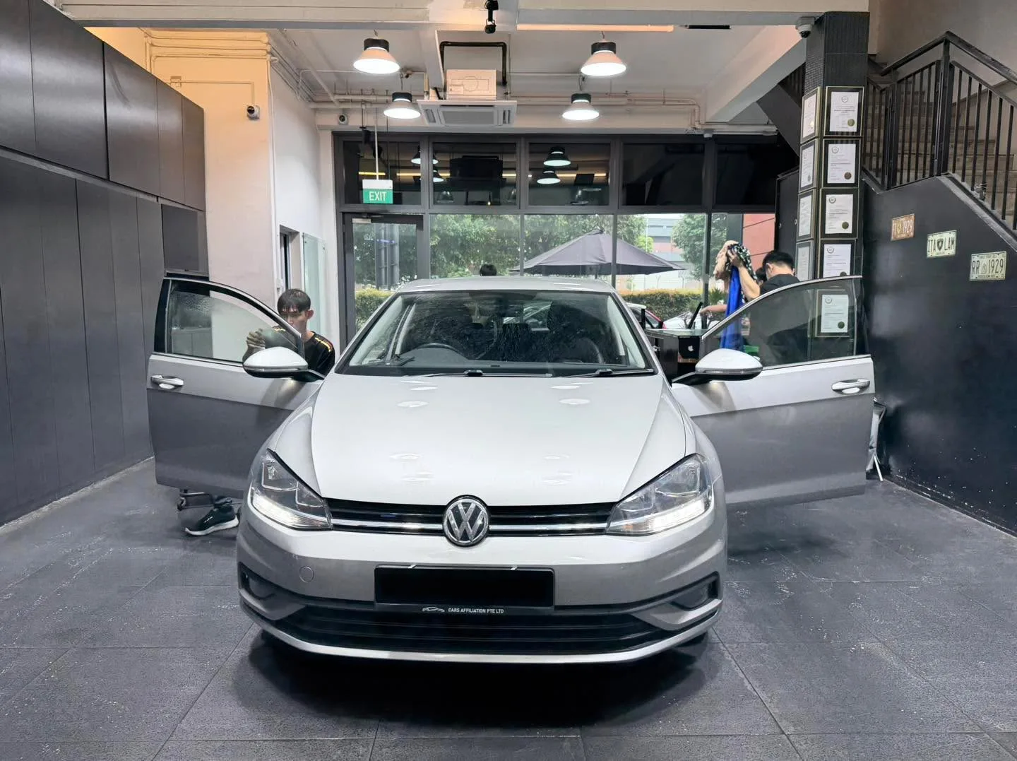 A Tesla Model 3 with doors open, viewed in profile inside the workshop during tinting work.