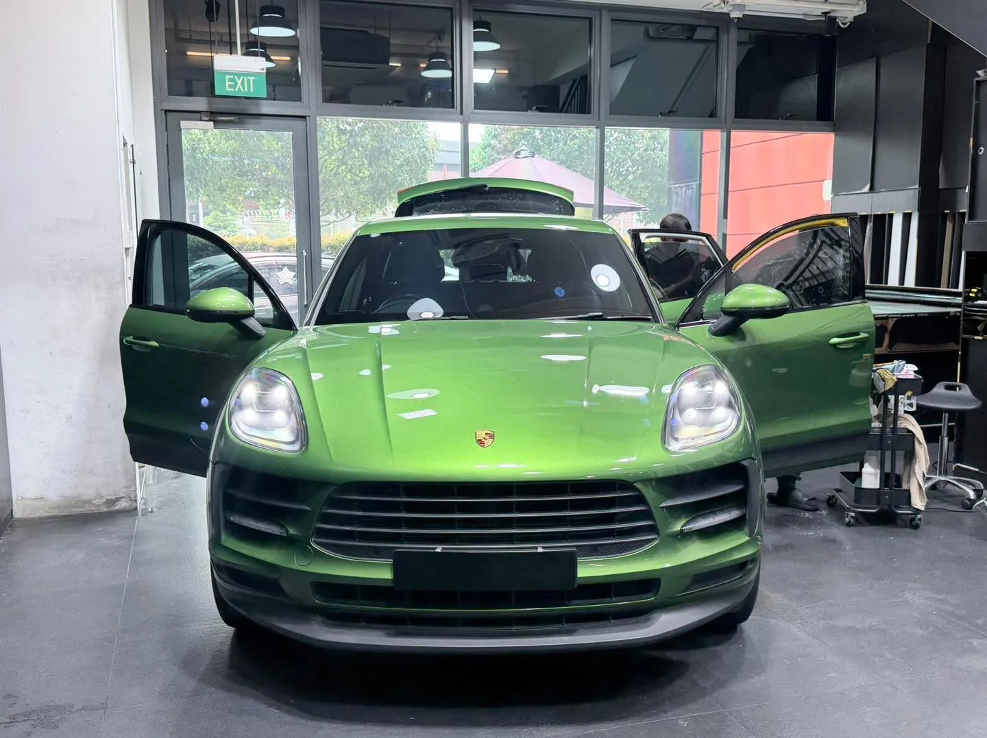 A bright green Porsche Macan S with both doors open, facing the camera in the workshop.
