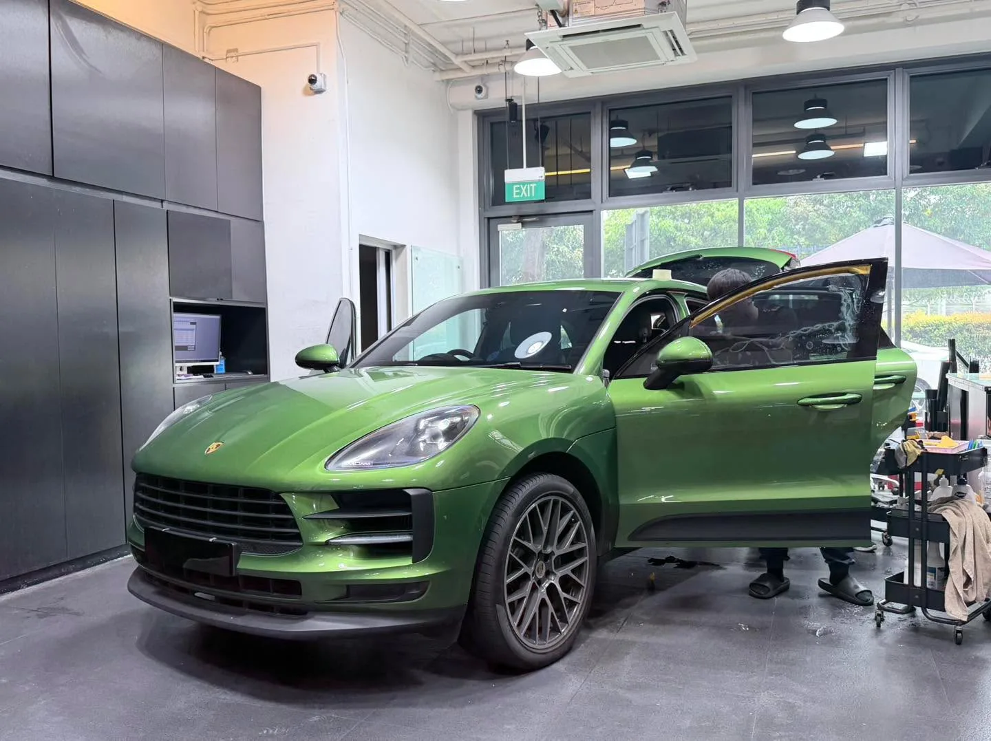 A bright green Porsche Macan S in profile with driver door open, doors visible, in the workshop.