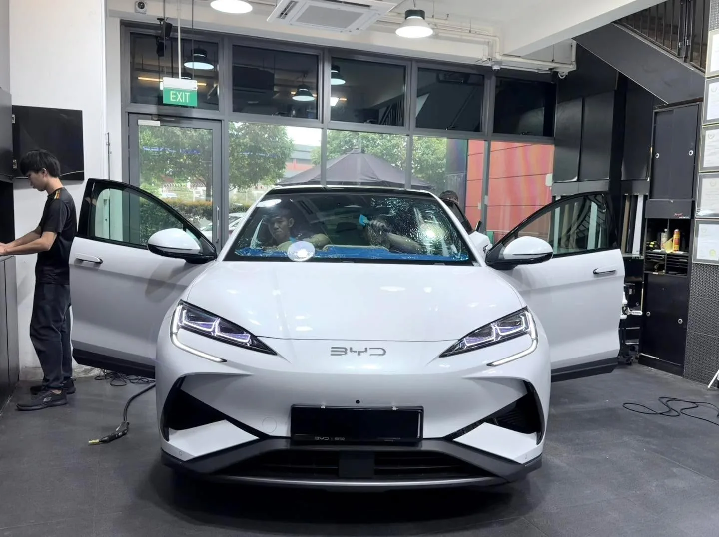 A white BYD Sealion 7 with doors open, staff working, in the workshop.