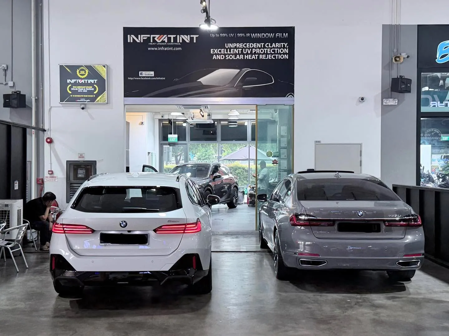 A white BMW sedan and a grey BMW sedan parked indoors at the workshop.