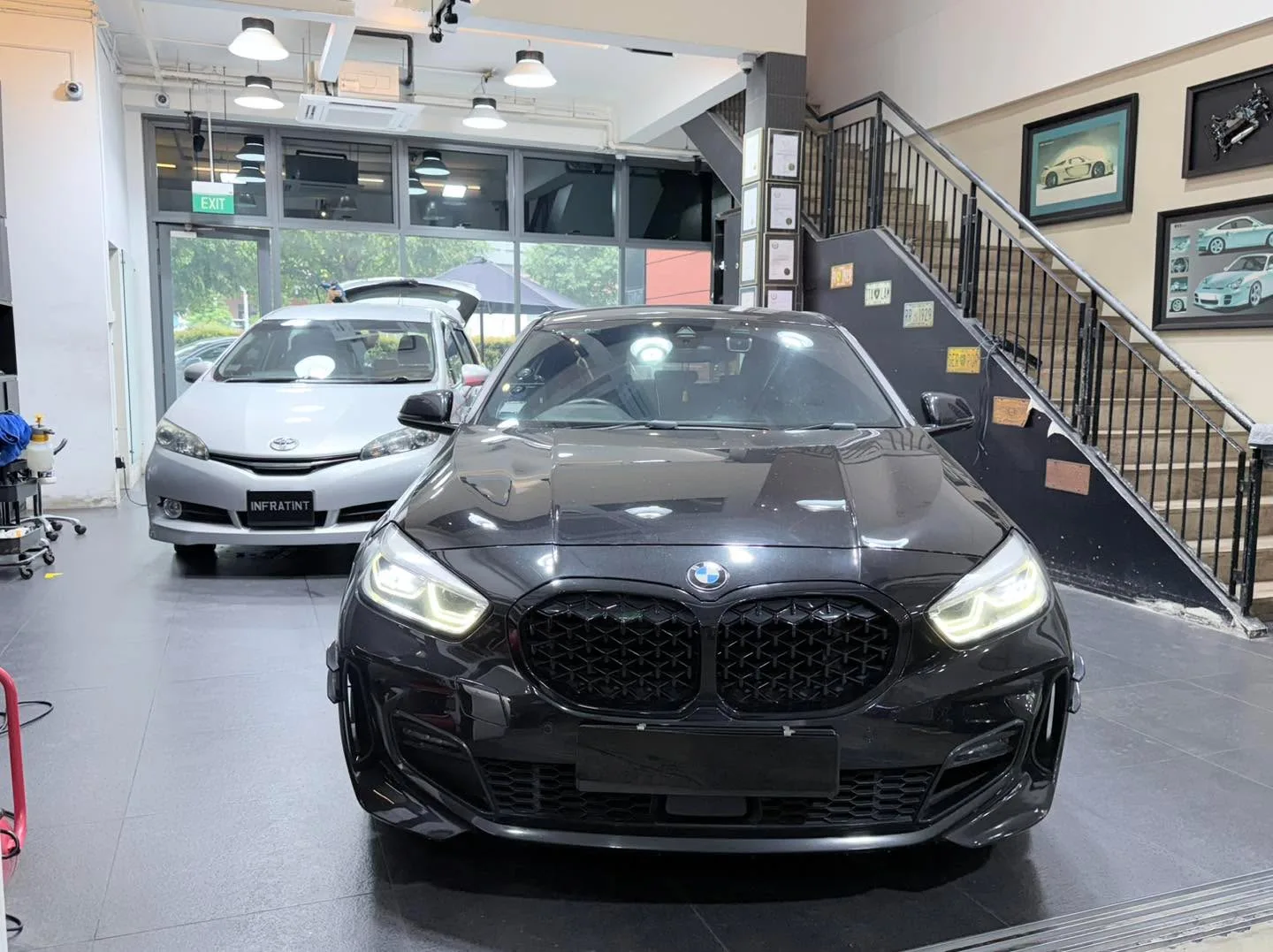 A black BMW compact car photographed head-on inside the workshop.