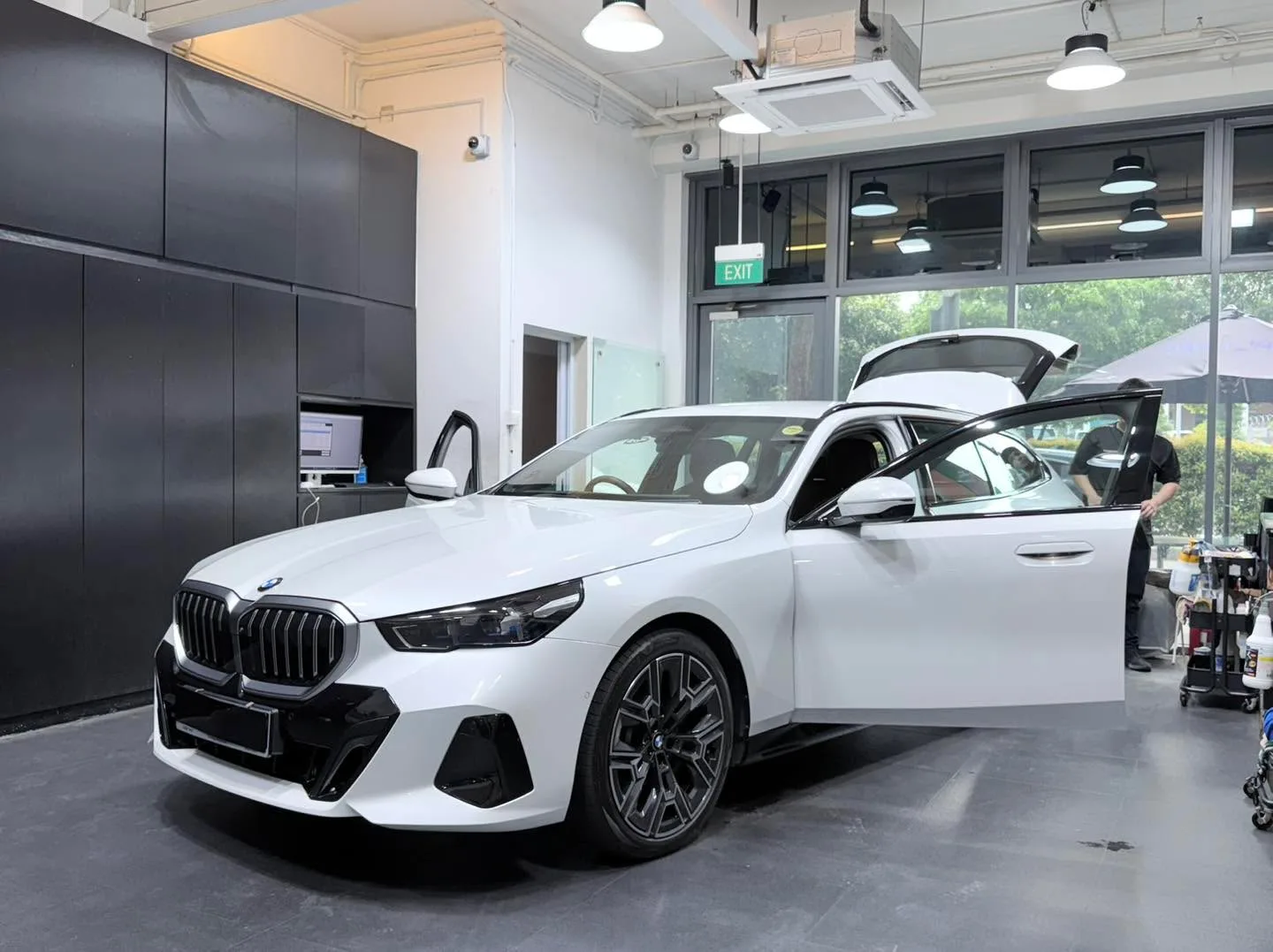 A white BMW compact car with doors open inside the workshop during tinting.
