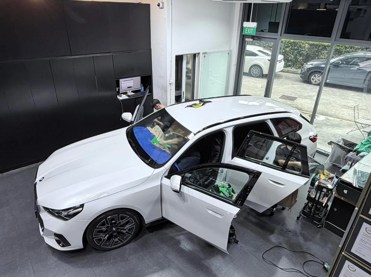 A white Toyota hatchback with doors open during window tinting at the workshop.