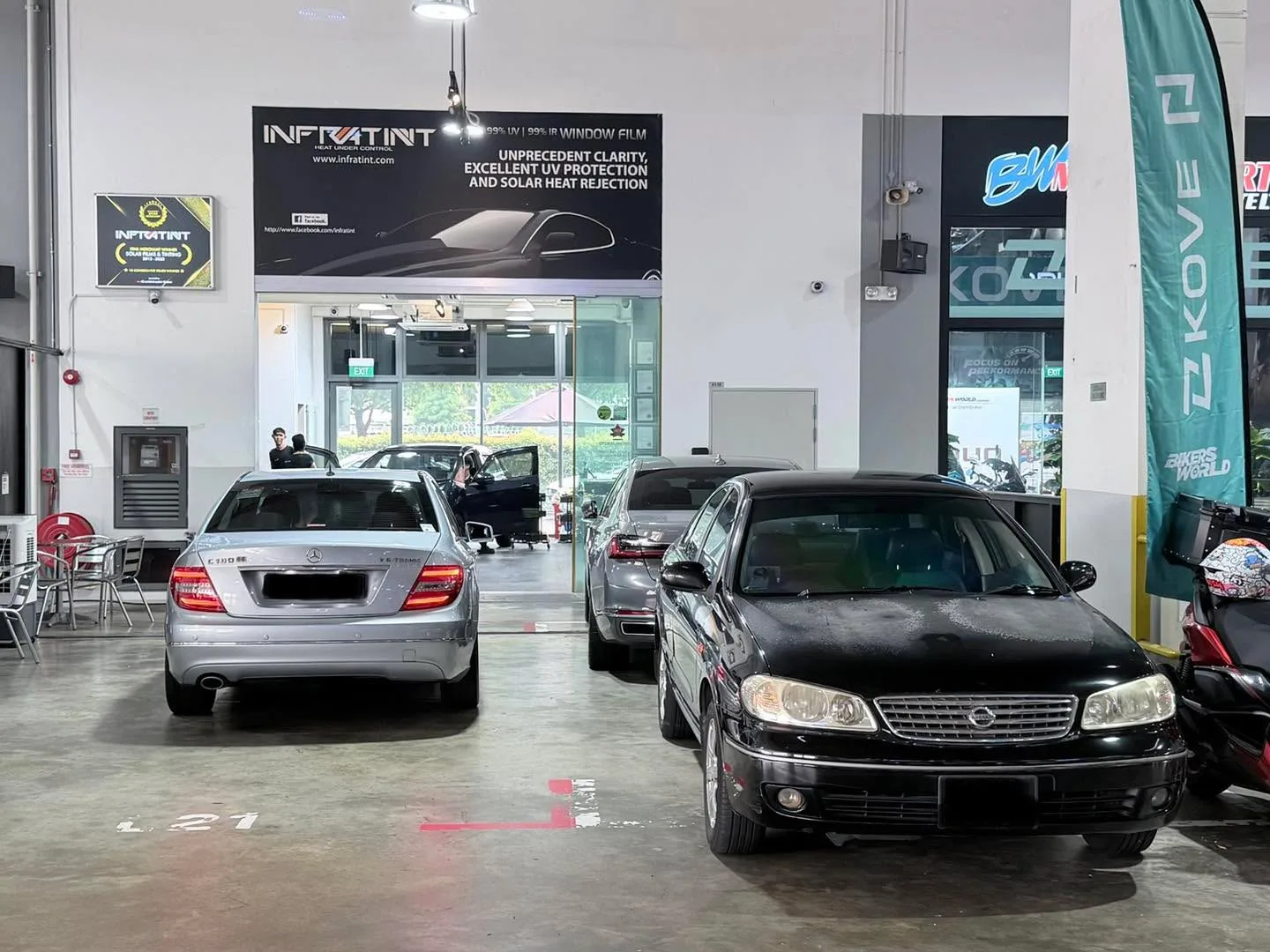 A silver Nissan sedan and a black Nissan sedan parked in the workshop.