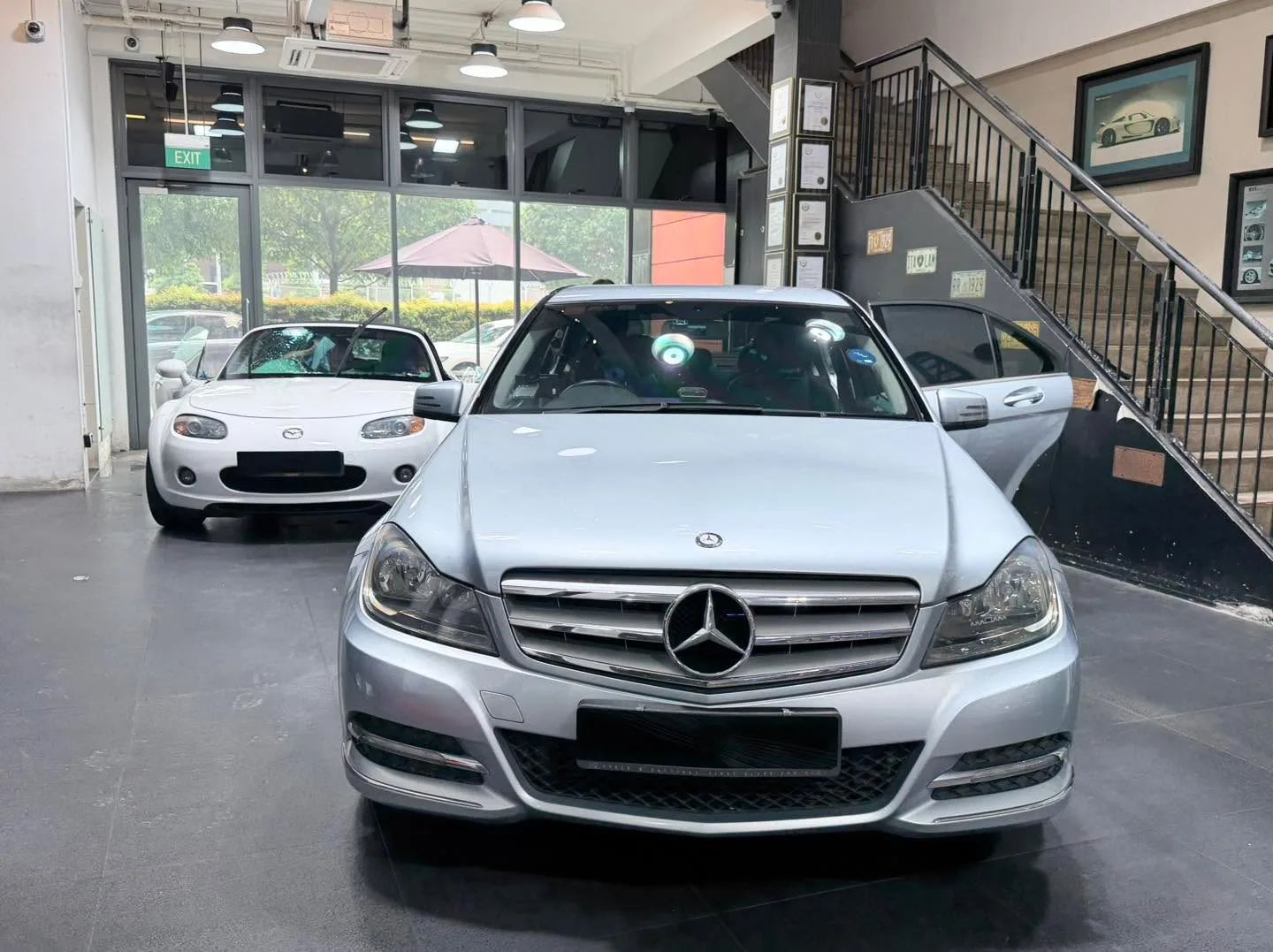 A silver Mercedes-Benz C-Class sedan and a white Mazda MX-5 convertible in the workshop.