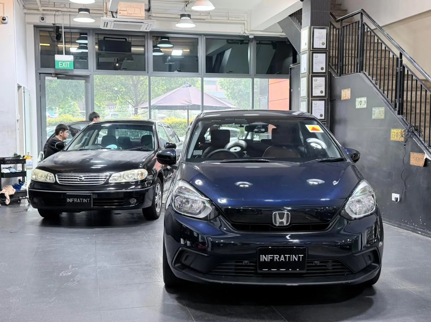 A black Honda Jazz hatchback and a black Nissan sedan undergoing tinting work.